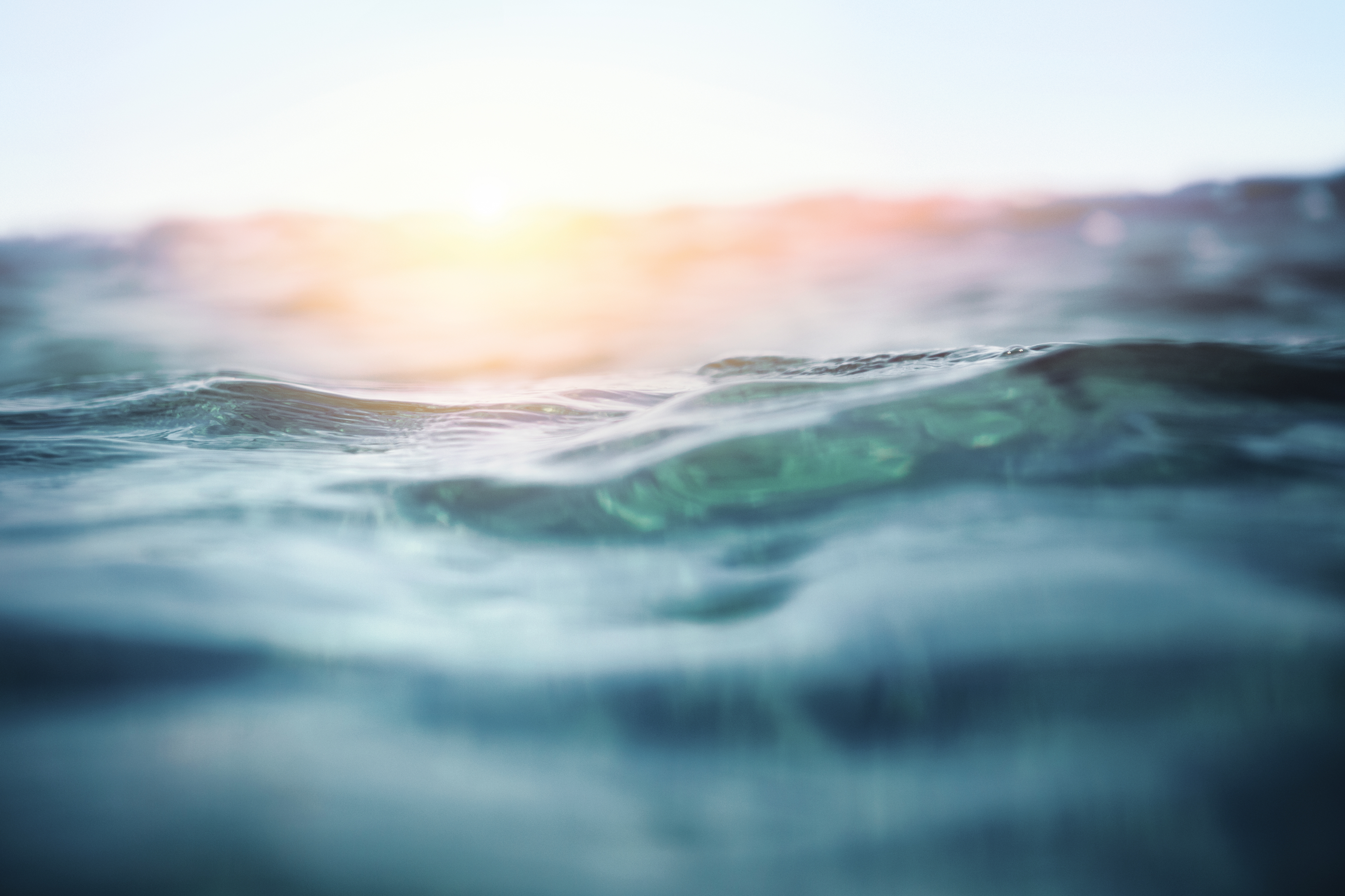 Wellen im Meer bei Sonnenuntergang, blaues Wasser, sanftes Licht.