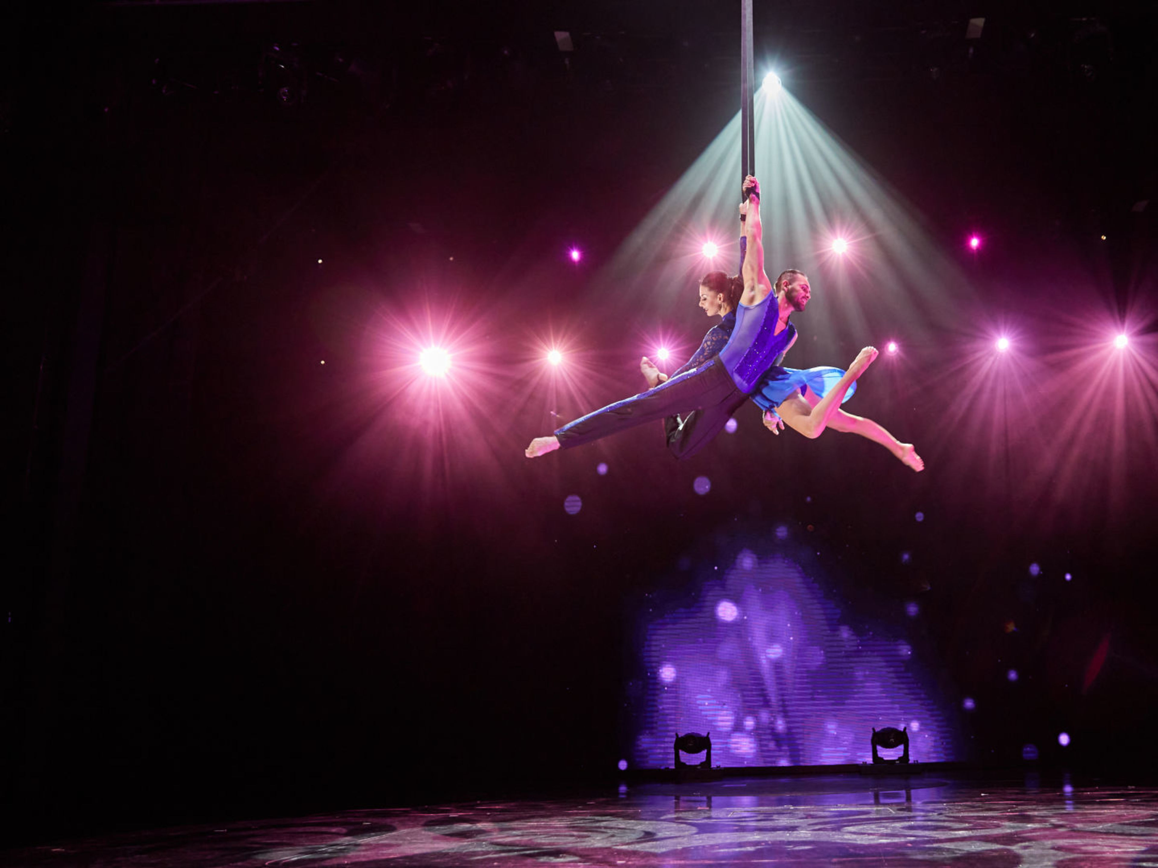 Show an Bord - Entertainment Zwei Akrobaten in blauen Kostümen schweben unter bunten Lichtern.