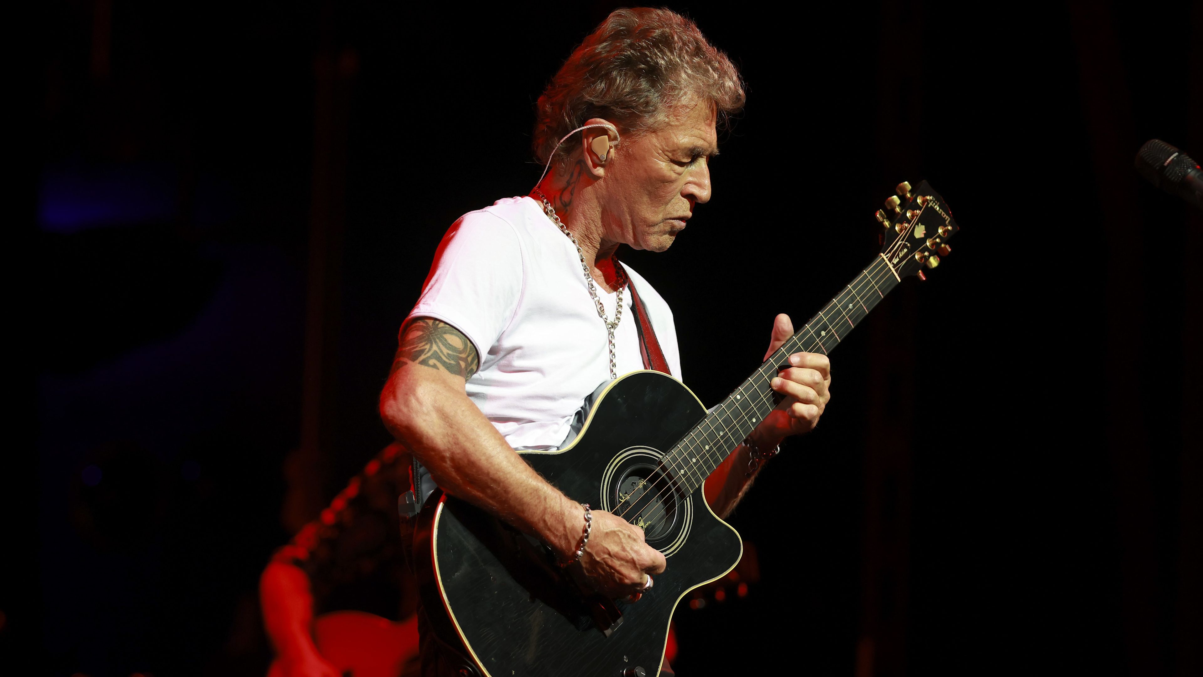 Mann spielt Gitarre auf Bühne, trägt weißes T-Shirt. Mann spielt Gitarre auf Bühne, trägt weißes T-Shirt.