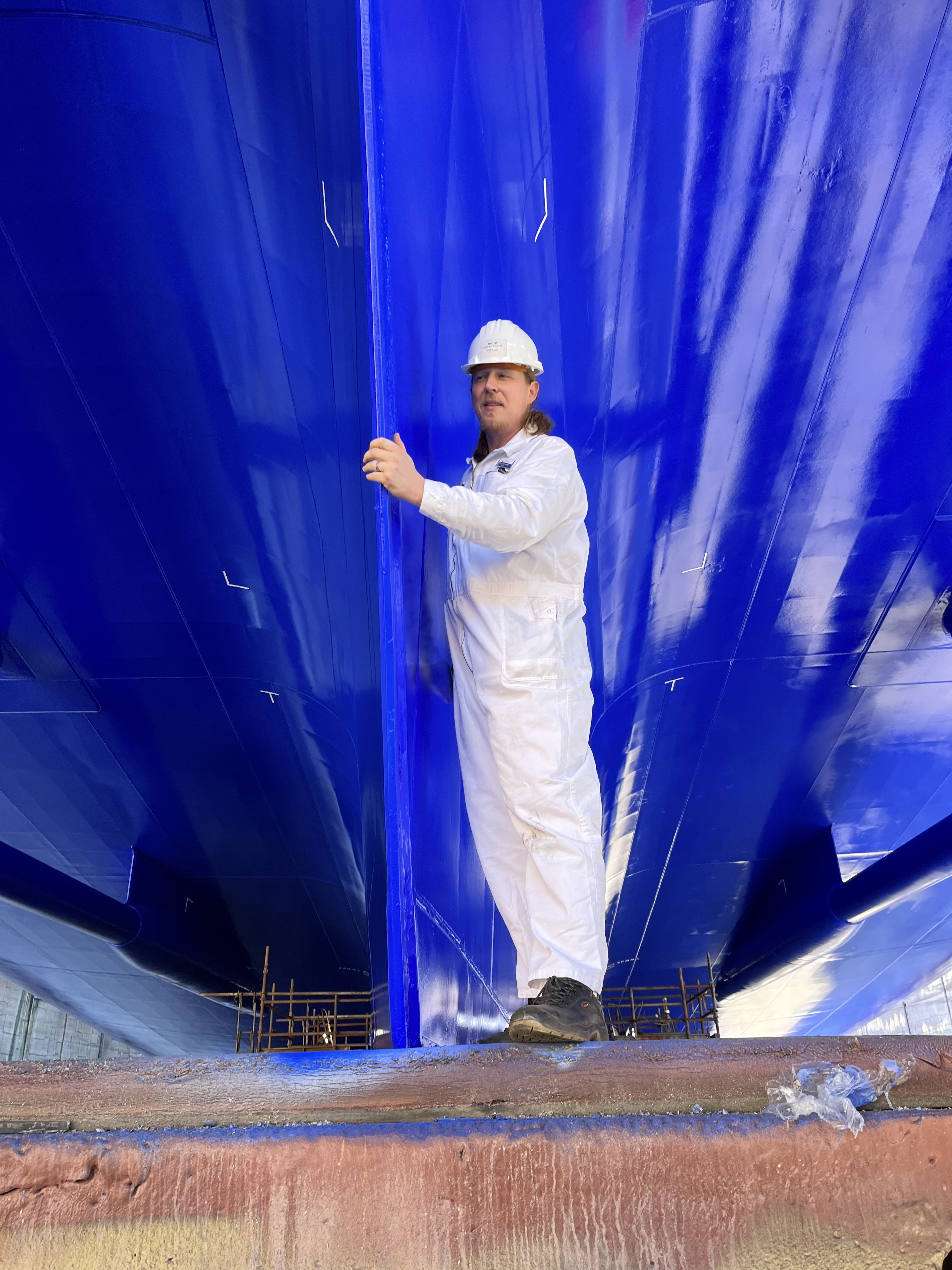 Mann in weißem Overall unter blauem Schiffsrumpf.