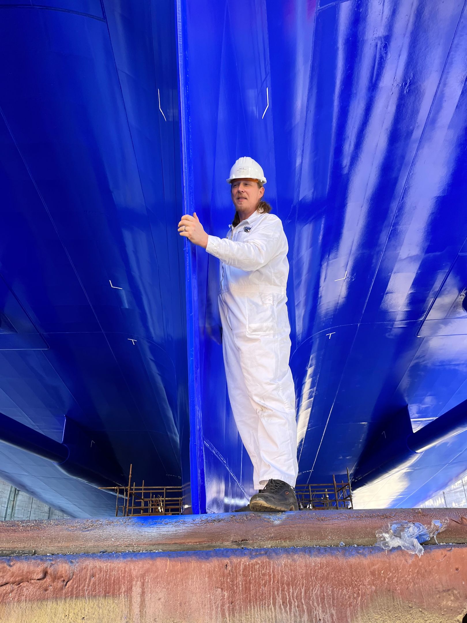 Mann in weißem Overall unter blauem Schiffsrumpf.
