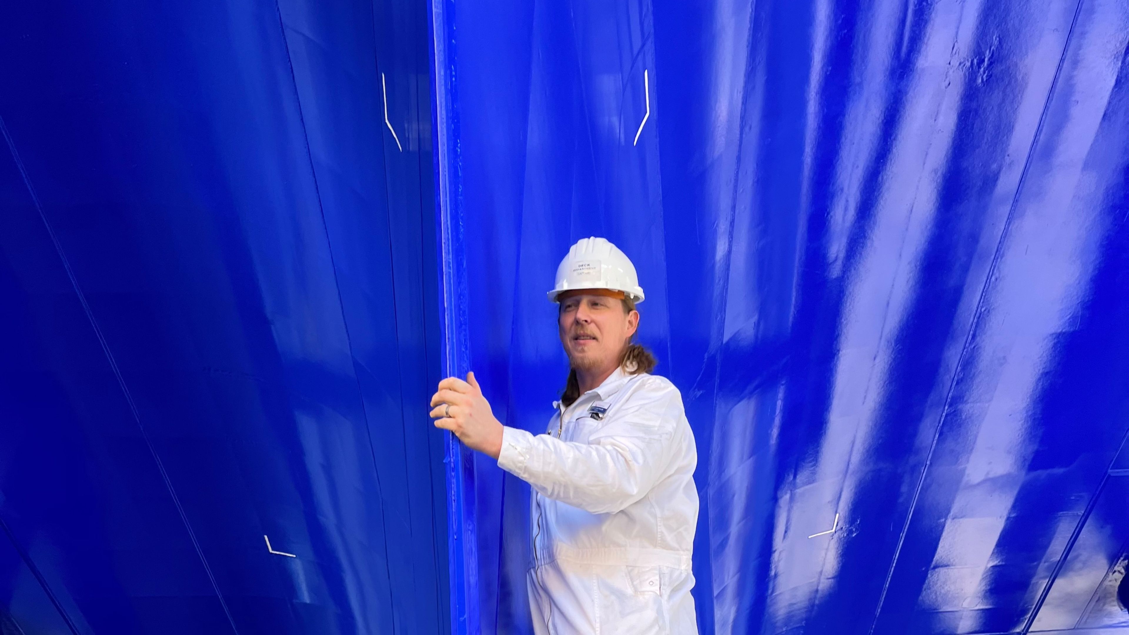 Kapitän Hilko Tjard Mahler Mann in weißem Overall unter blauem Schiffsrumpf.