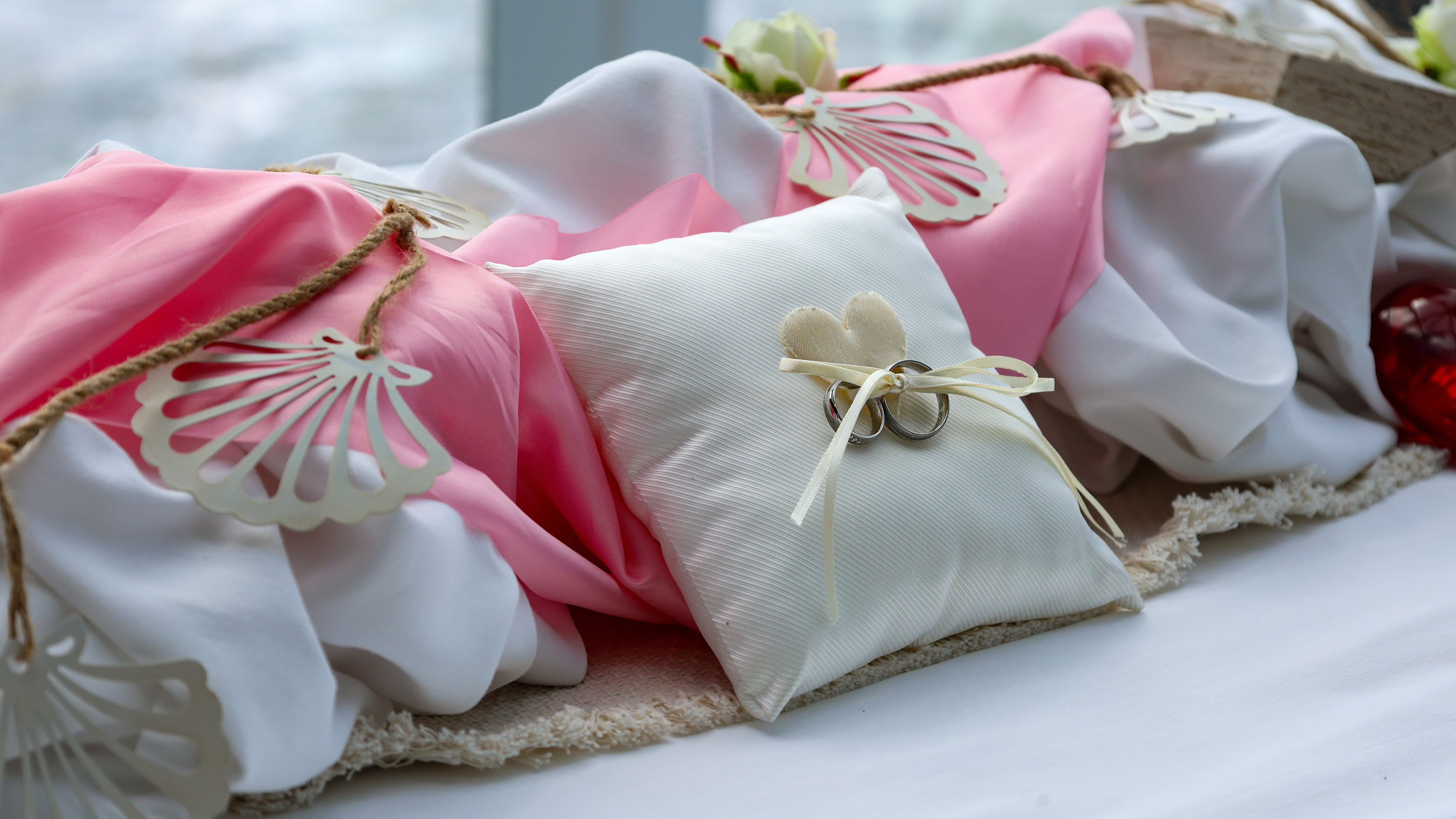 Weiße Kissen mit Eheringen, rosa Stoff, Muschel-Dekoration.