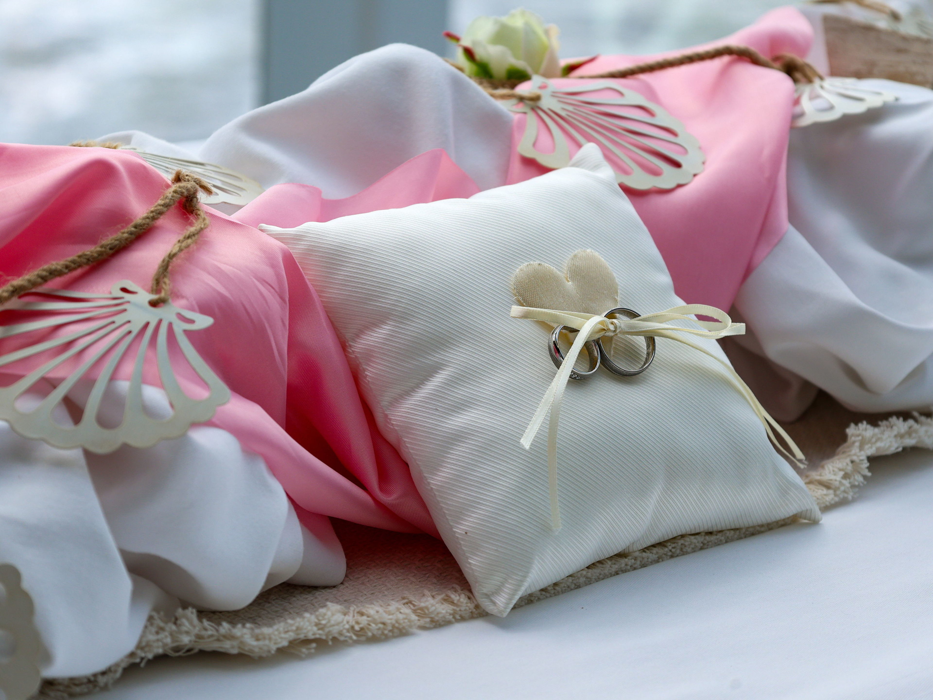 Weiße Kissen mit Eheringen, rosa Stoff, Muschel-Dekoration. Weiße Kissen mit Eheringen, rosa Stoff, Muschel-Dekoration.