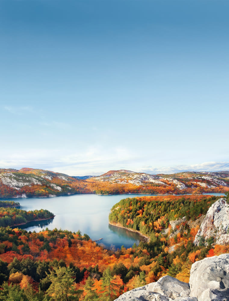 Herbstliche Landschaft mit See, bunten Bäumen und Bergen unter klarem Himmel.