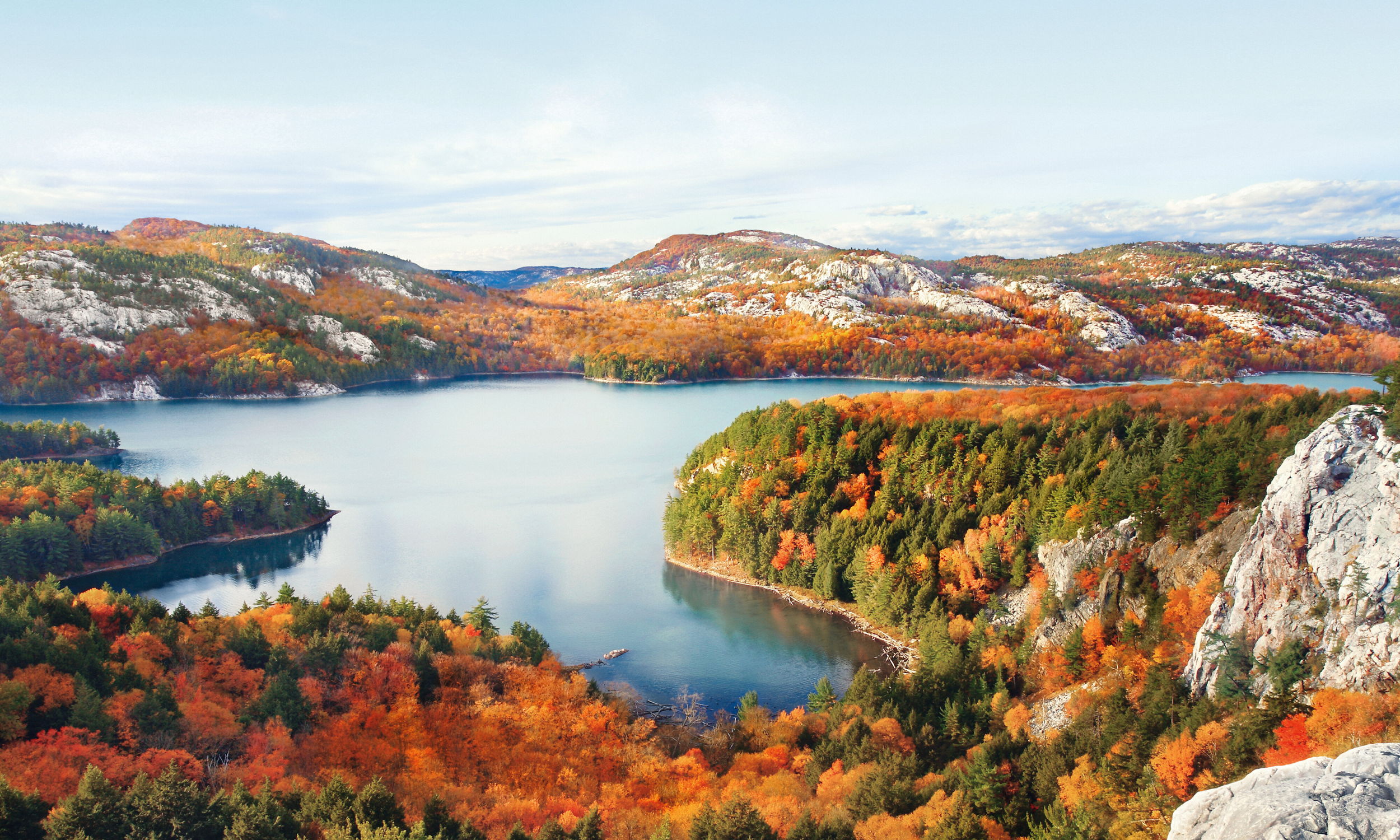 Herbstliche Landschaft mit See, bunten Bäumen und Bergen unter klarem Himmel.