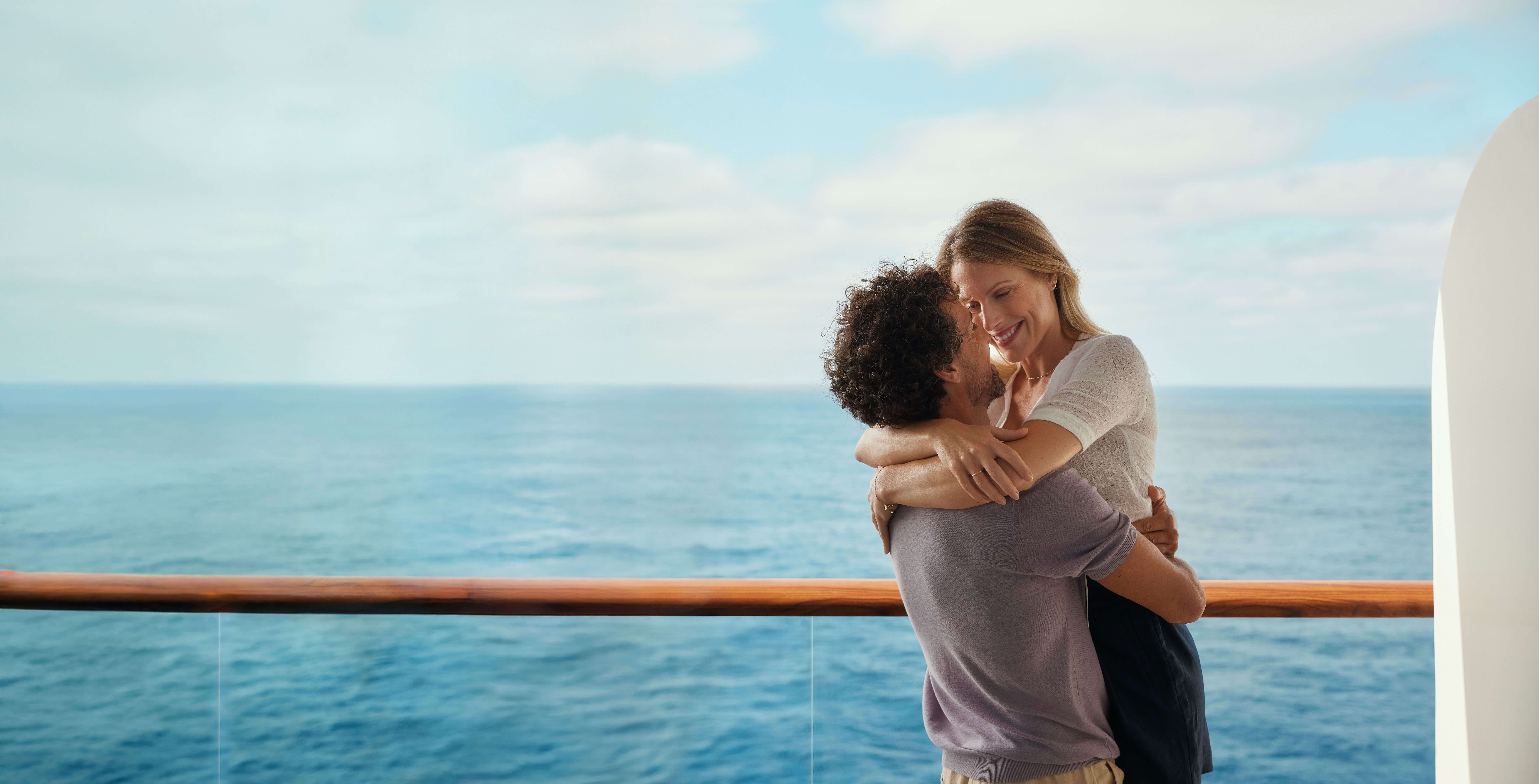 Paar umarmt sich auf Kreuzfahrtschiff, Meer im Hintergrund.