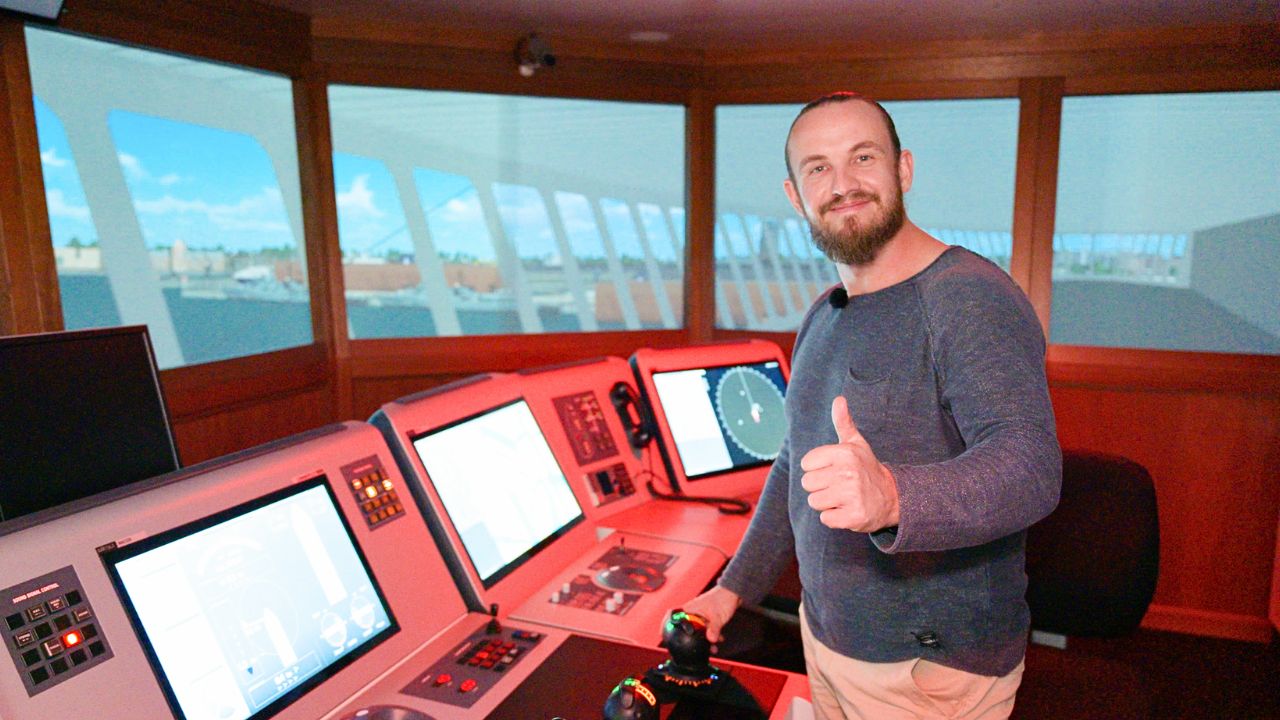 Mann im Schiffssteuerraum mit Daumen hoch, lächelnd.