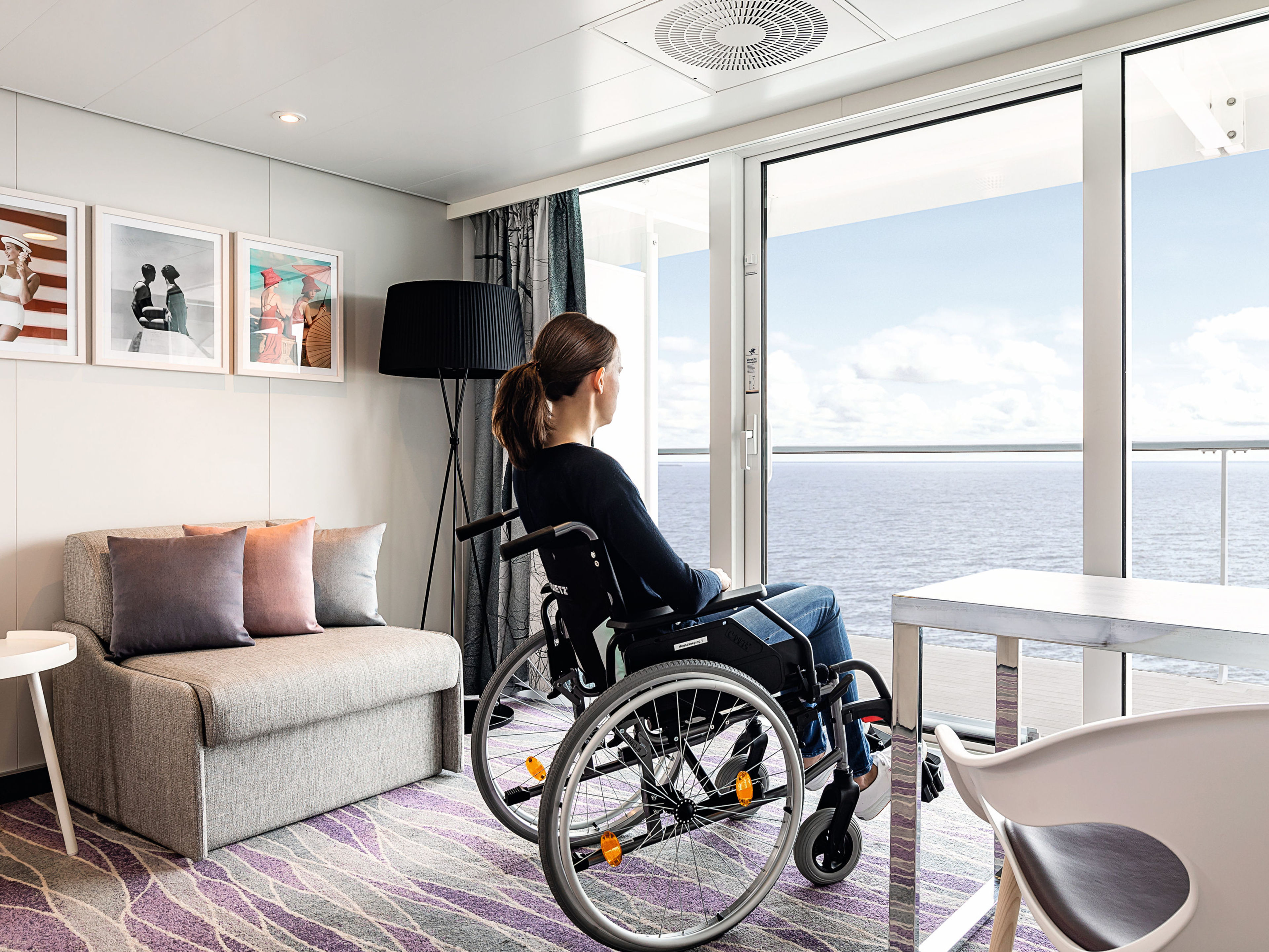 Frau im Rollstuhl in einer barrierefreien Suite Frau im Rollstuhl blickt aufs Meer durch Balkontür.