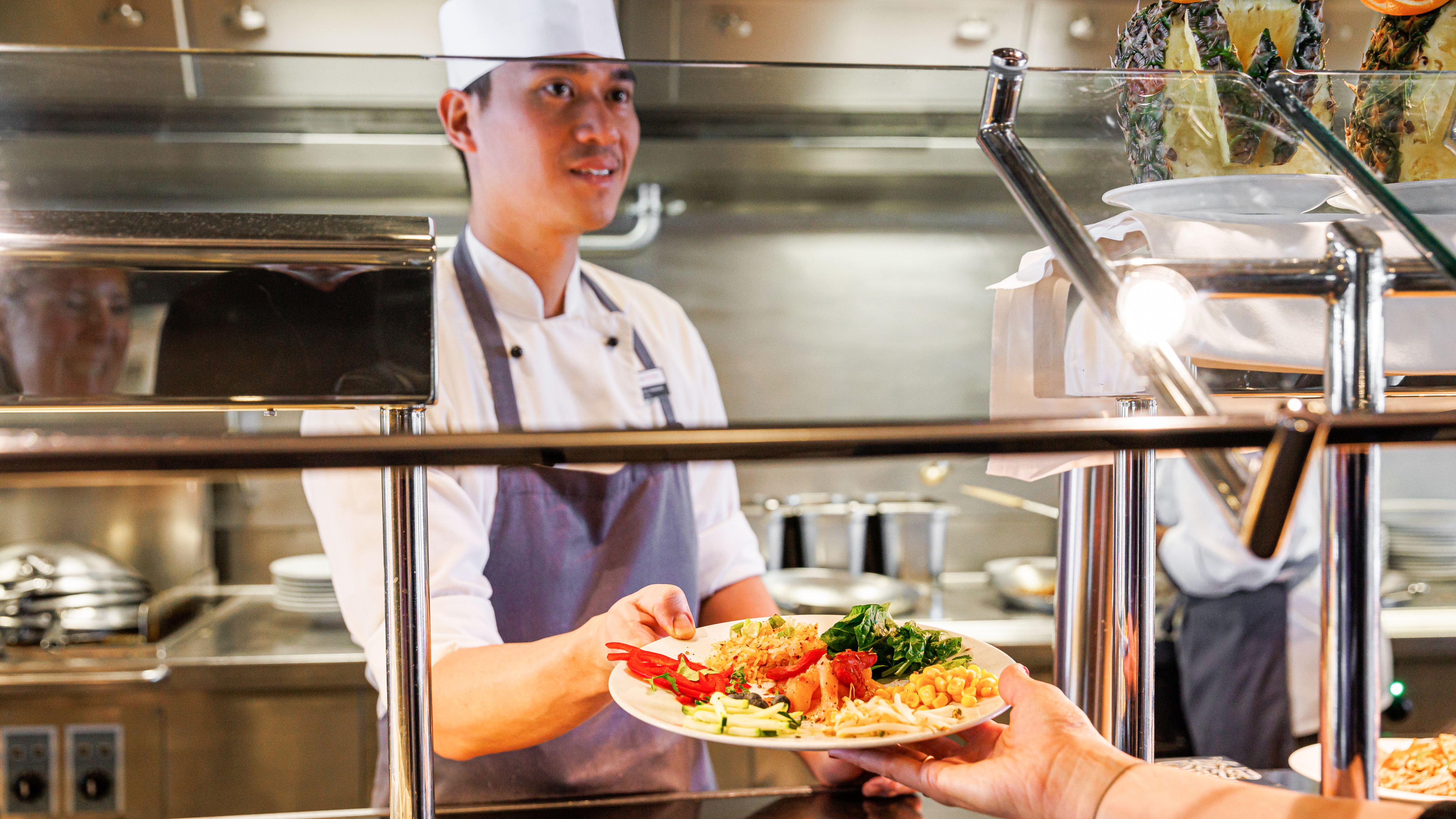 Koch serviert Teller mit Gemüse und Nudeln in Kantine.