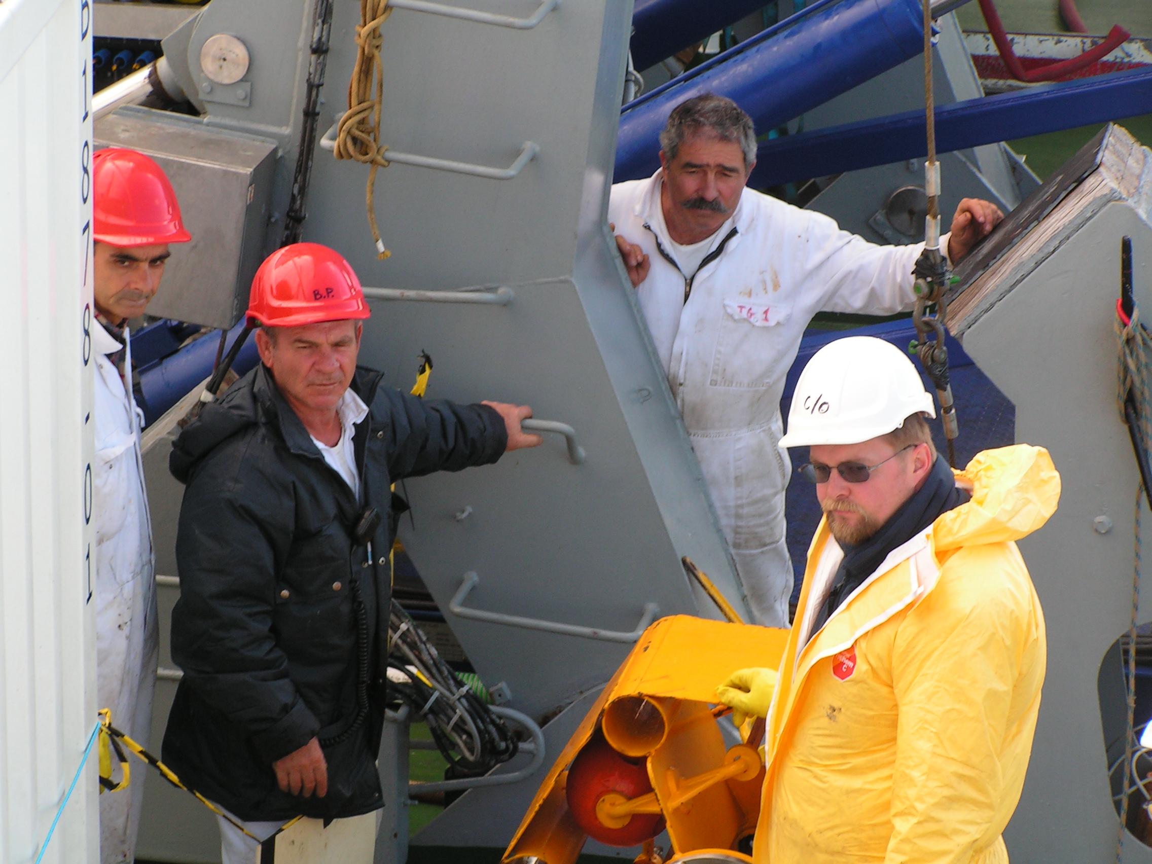 Arbeiter in Schutzkleidung und Helmen auf einem Schiff.