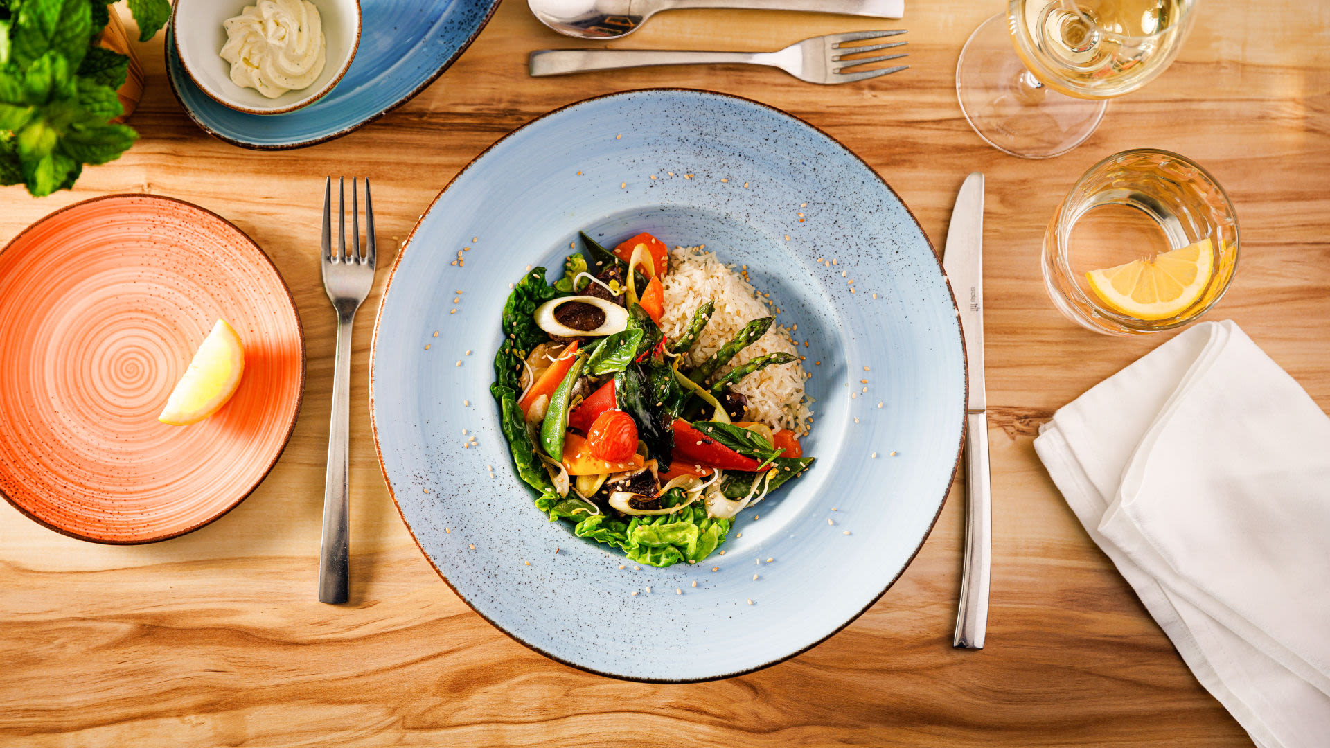 Bunter Salat mit Reis auf blauem Teller, Holztisch.