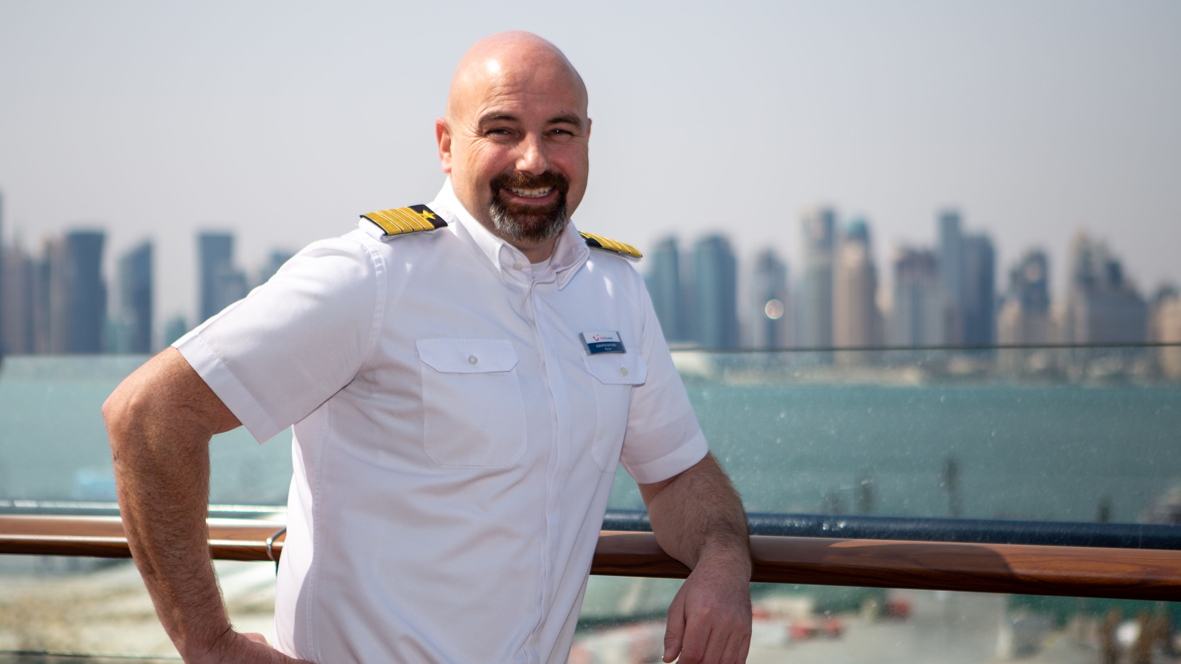Günter Batzner Mann in weißer Uniform auf Kreuzfahrtschiff, Skyline im Hintergrund.
