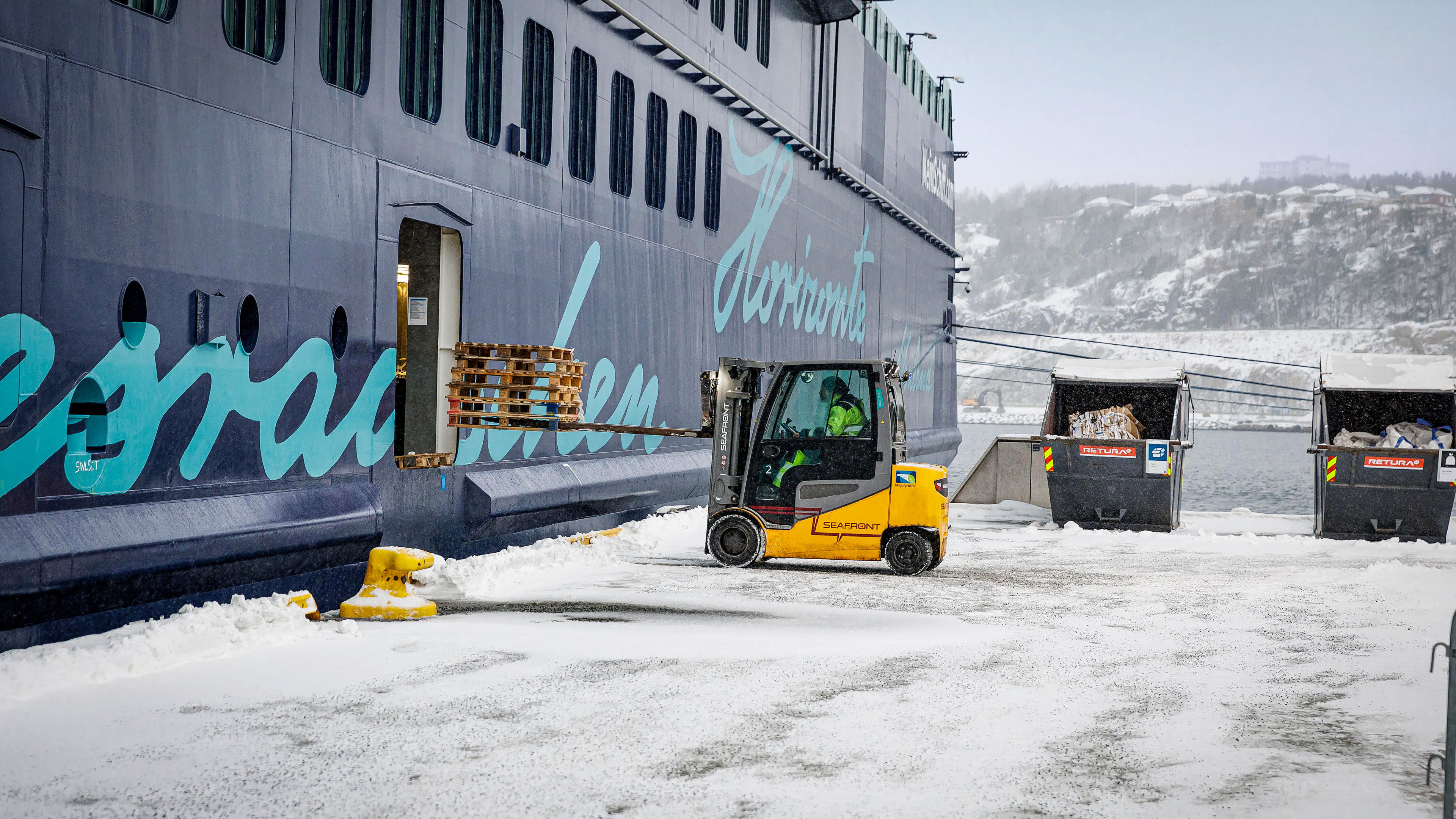 Gabelstapler lädt Paletten auf Kreuzfahrtschiff im Schnee.