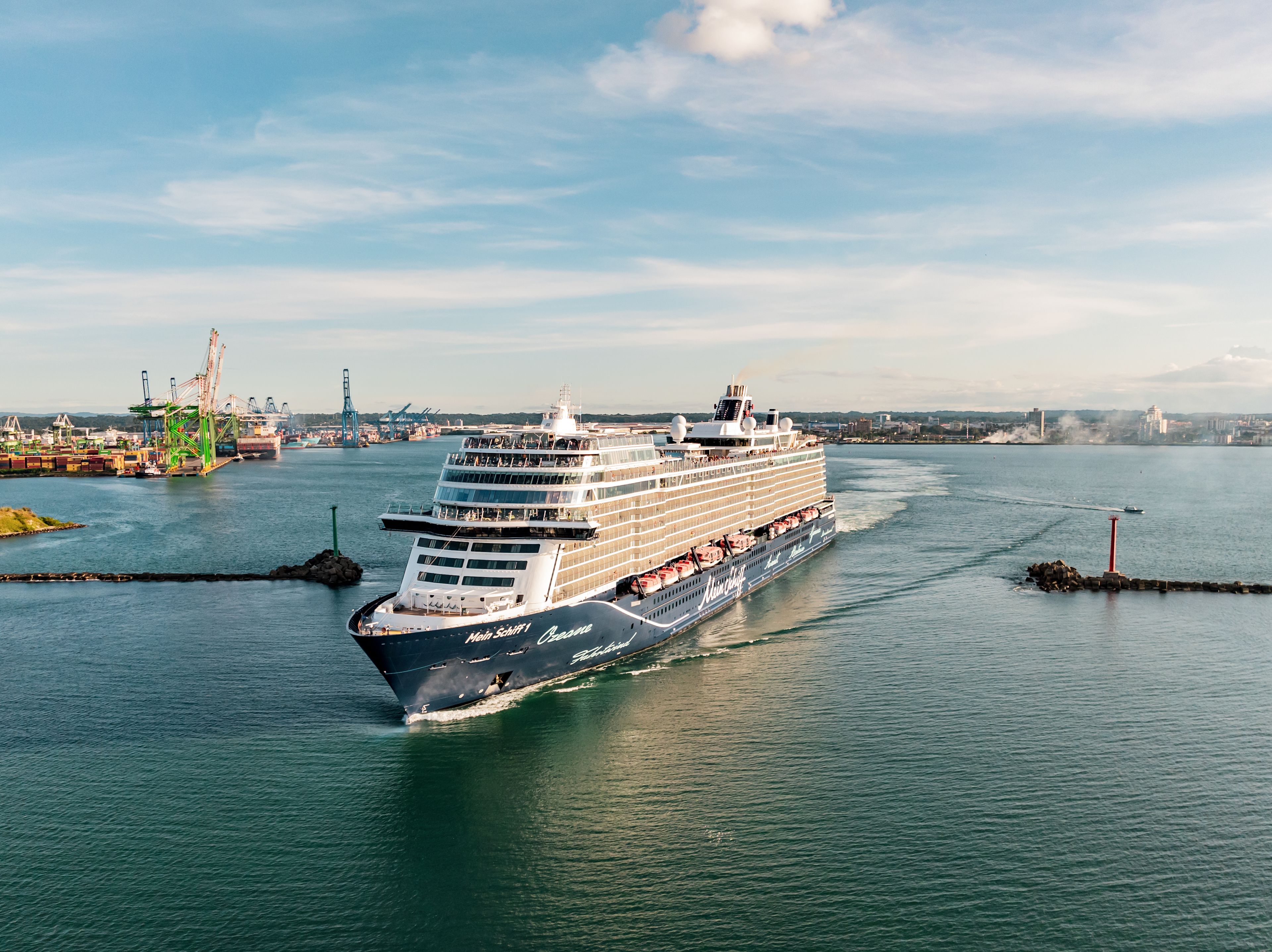 Kreuzfahrtschiff der Mein Schiff® Flotte im Hafen, blauer Himmel.