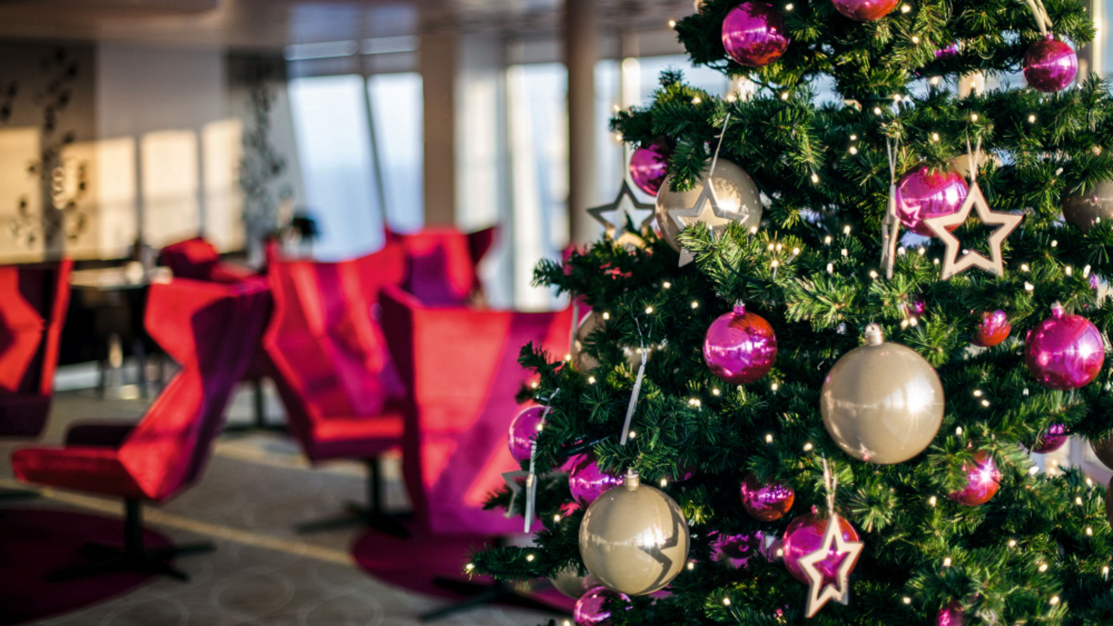 Weihnachtsbaum mit rosa Kugeln und Sternen, rote Stühle im Hintergrund. Weihnachtsbaum mit rosa Kugeln und Sternen, rote Stühle im Hintergrund.