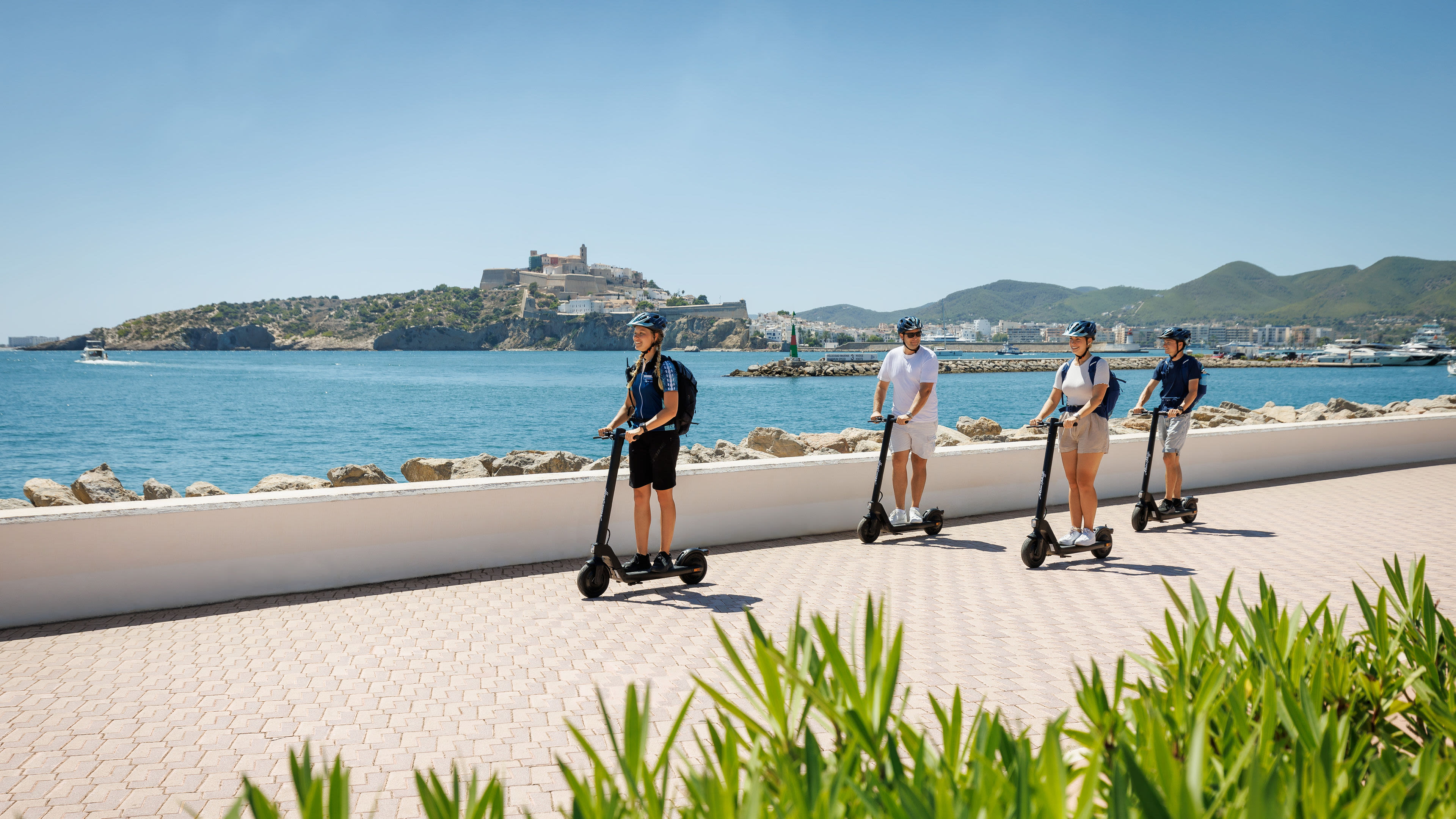 Vier Personen fahren E-Scooter entlang der Küste von Ibiza.