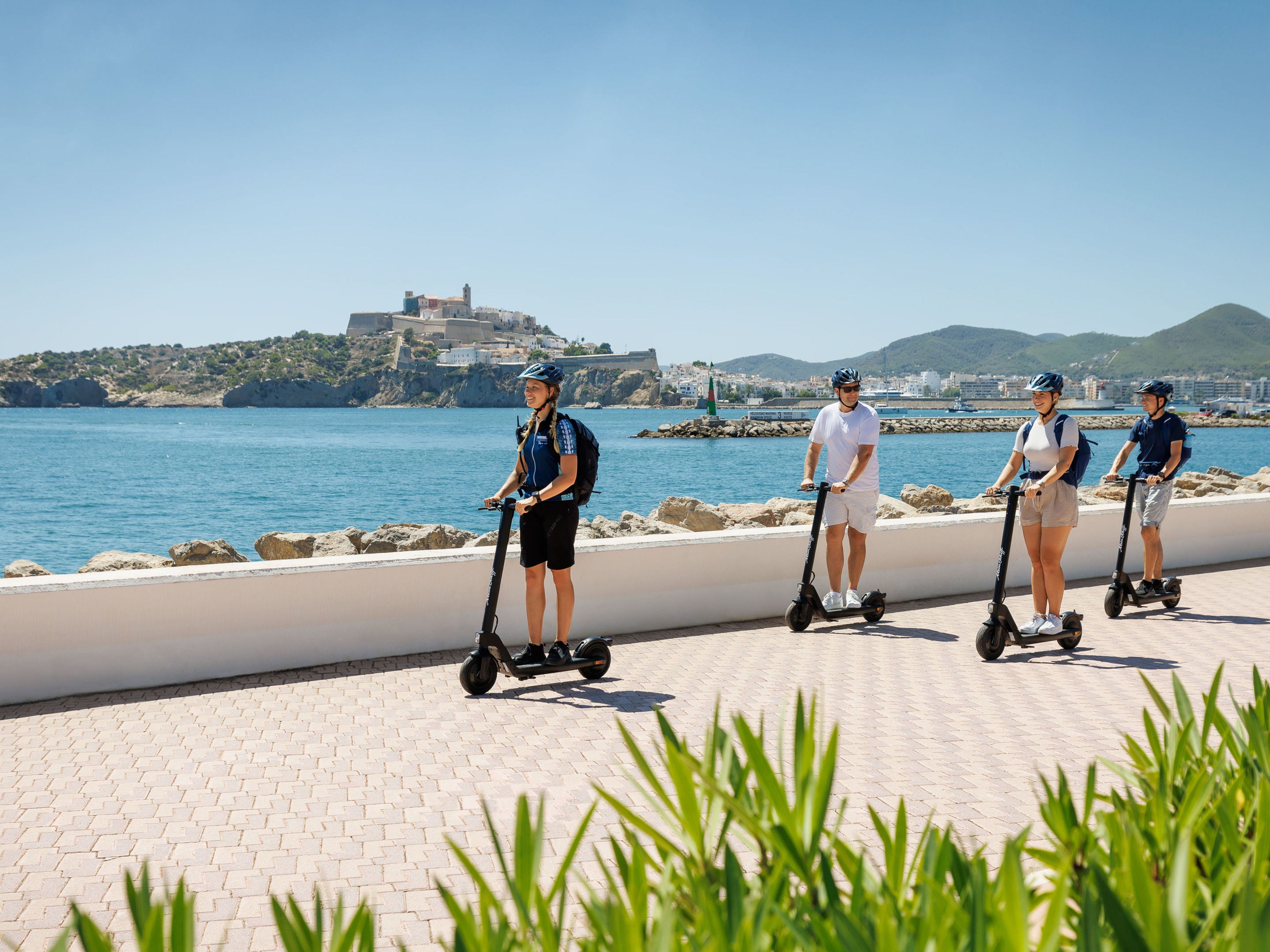 Vier Personen fahren E-Scooter entlang der Küste von Ibiza. Vier Personen fahren E-Scooter entlang der Küste von Ibiza.