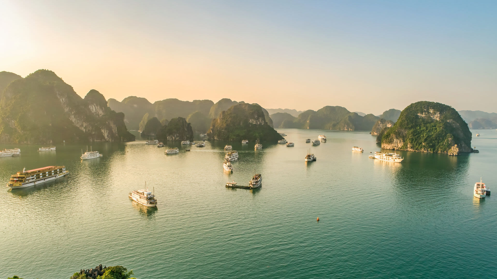 Boote in der Halong-Bucht bei Sonnenuntergang, umgeben von Kalksteinfelsen.