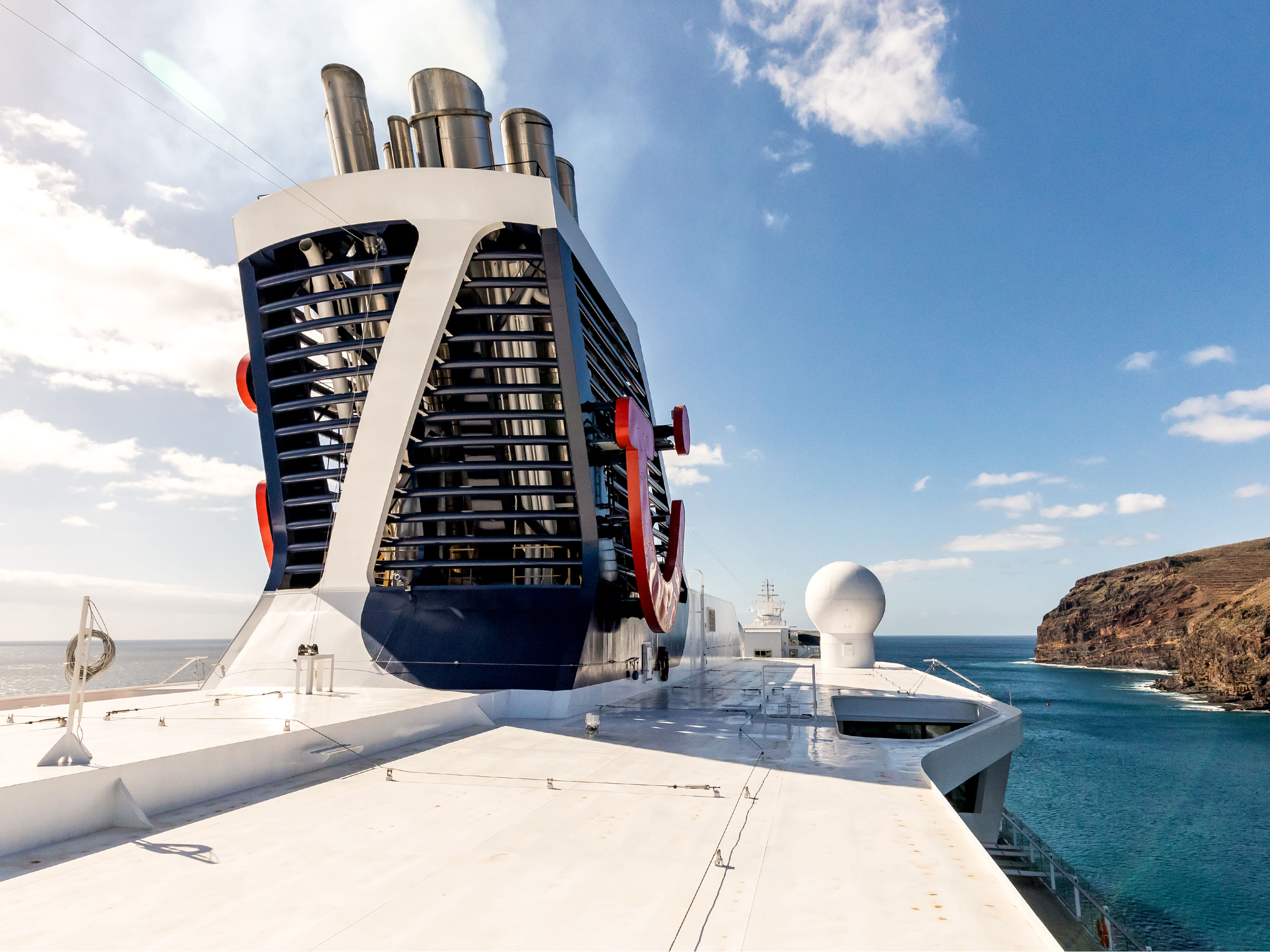 Nachhaltigkeit - Klimaschutz & Emissionen Kreuzfahrtschiff der Mein Schiff® Flotte vor felsiger Küste, blauer Himmel.