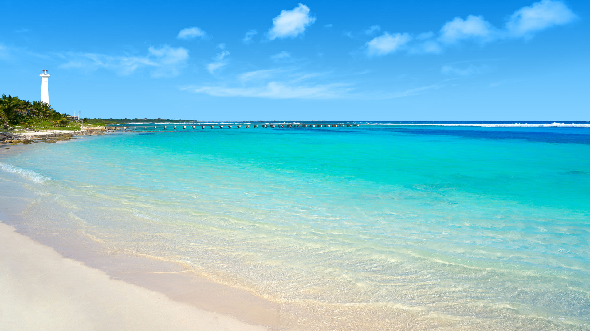 Strand mit türkisfarbenem Wasser, Leuchtturm und blauem Himmel.