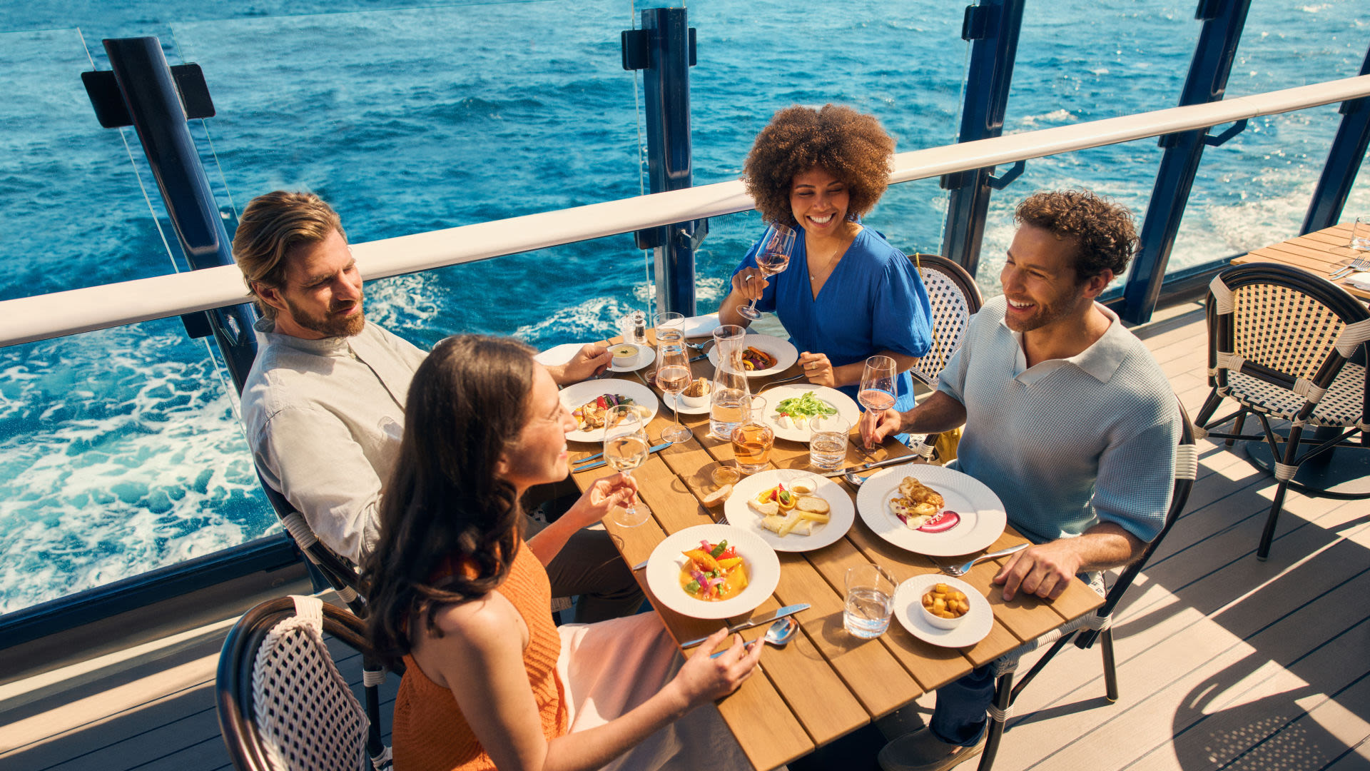 Freundesgruppe genießt ihr Essen im Außenbereich des Sur Mer Bistrots Vier Personen essen auf einem Kreuzfahrtschiff der Mein Schiff® Flotte mit Meerblick.