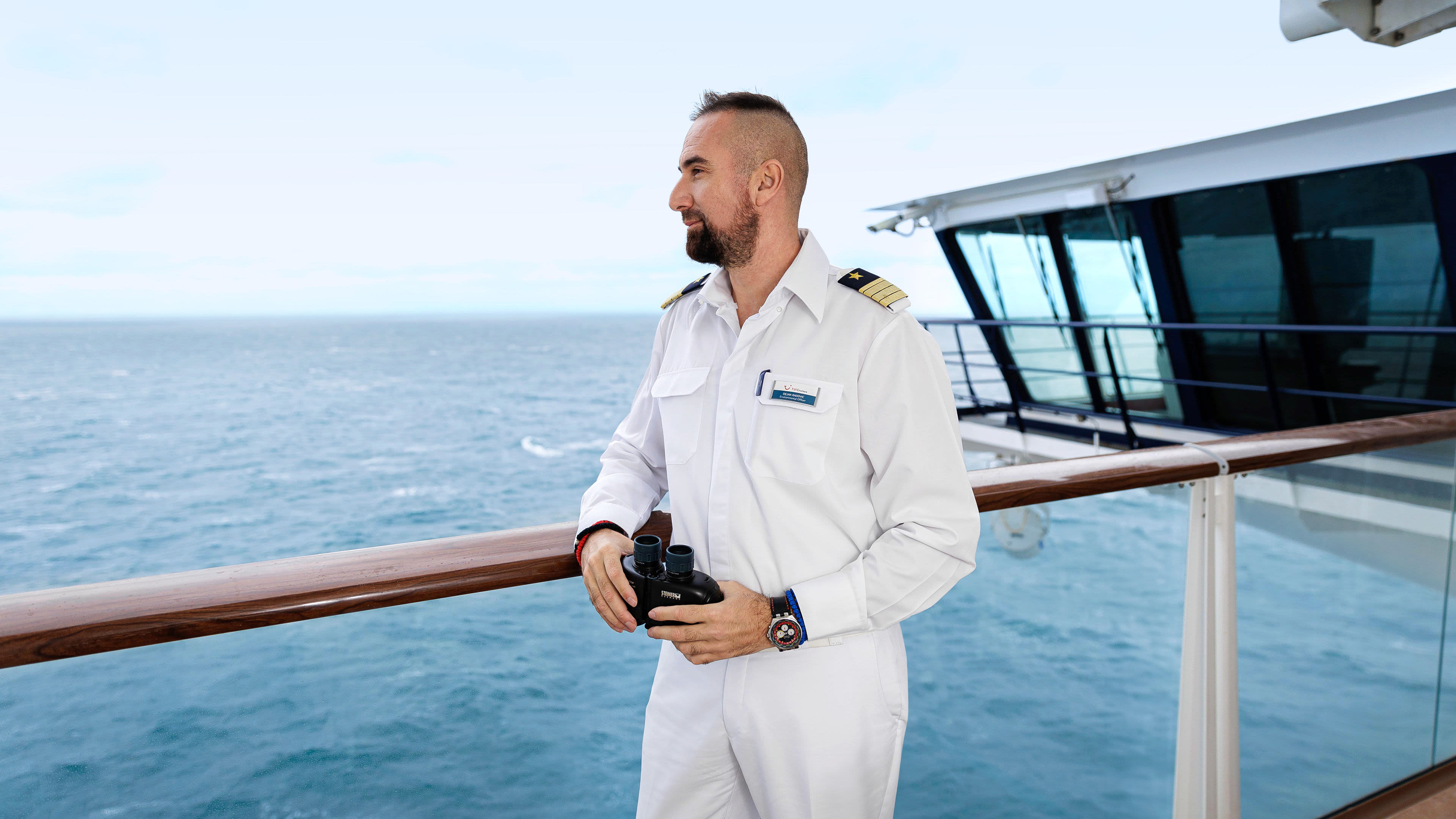 Mann in weißer Uniform mit Fernglas auf Kreuzfahrtschiff der Mein Schiff® Flotte.