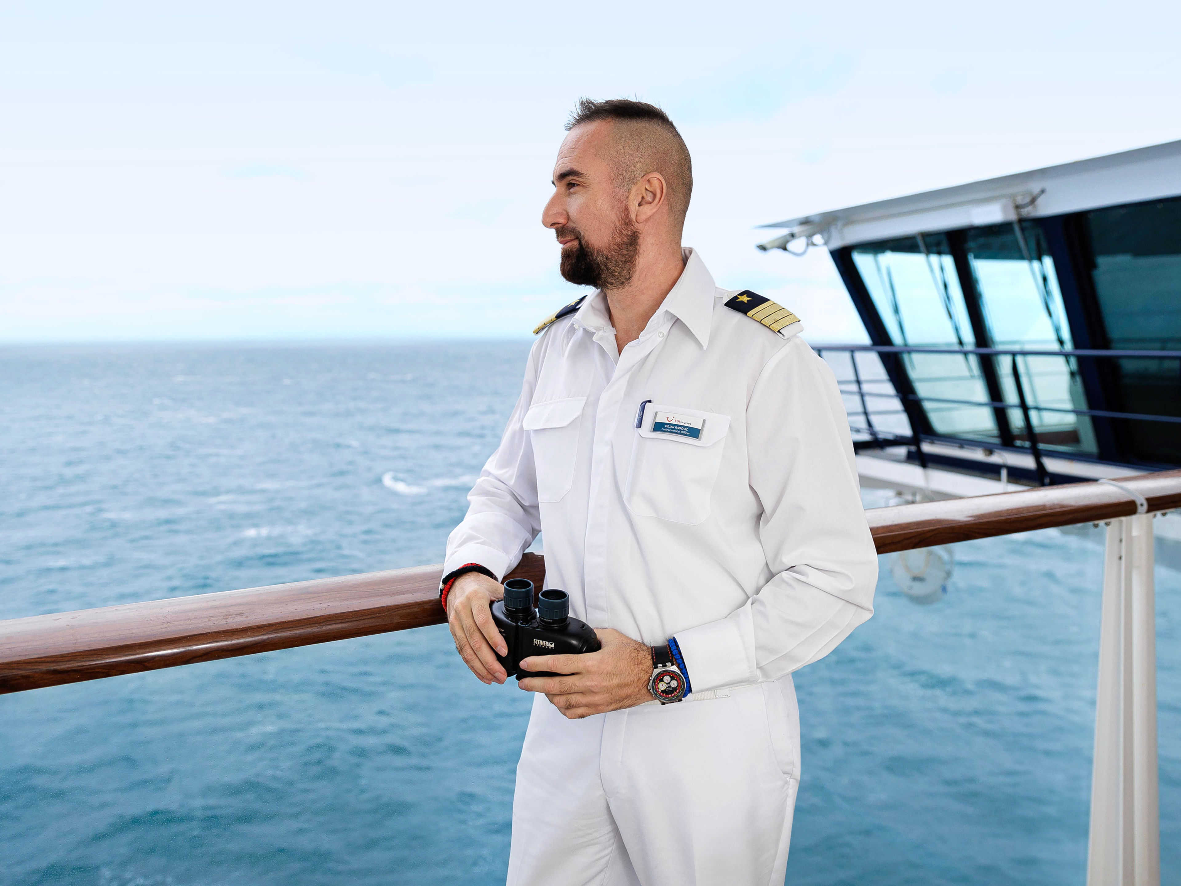 Nachhaltigkeit - Umweltoffizier Mann in weißer Uniform mit Fernglas auf Kreuzfahrtschiff der Mein Schiff® Flotte.