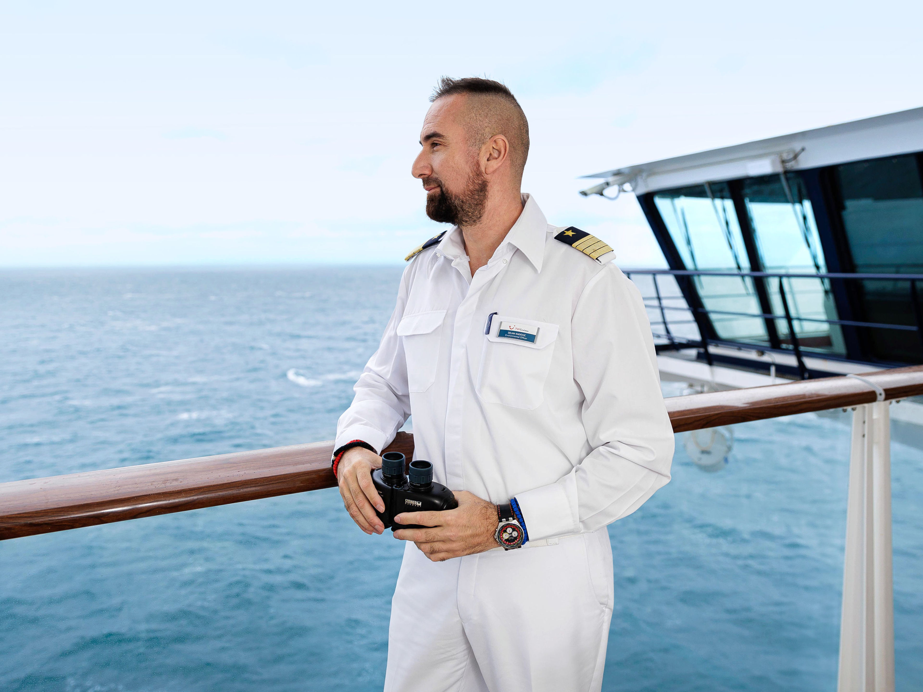 Mann in weißer Uniform mit Fernglas auf Kreuzfahrtschiff der Mein Schiff® Flotte. Mann in weißer Uniform mit Fernglas auf Kreuzfahrtschiff der Mein Schiff® Flotte.
