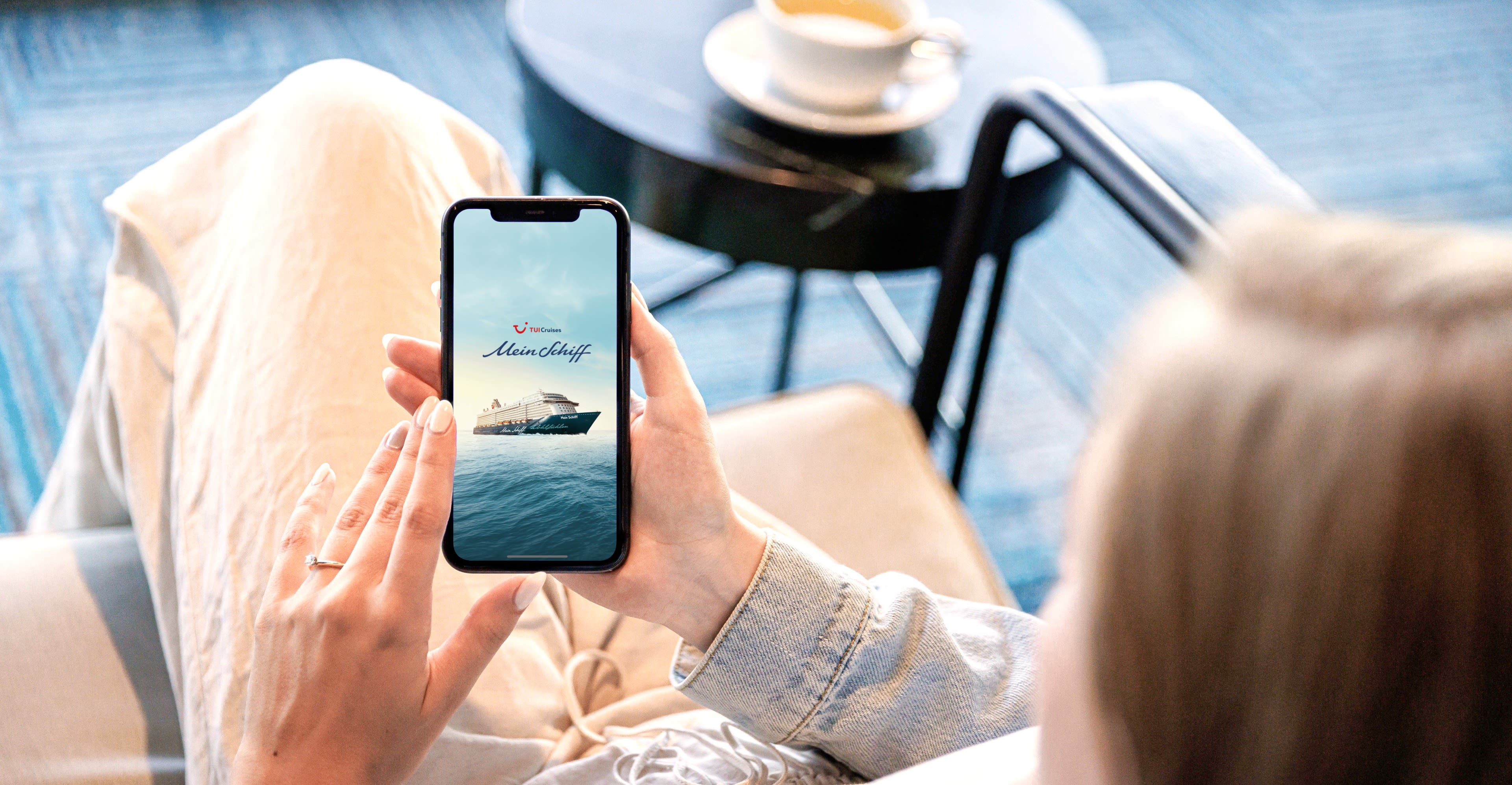 Mein Schiff App Frau betrachtet Kreuzfahrtschiff der Mein Schiff® Flotte auf Smartphone.