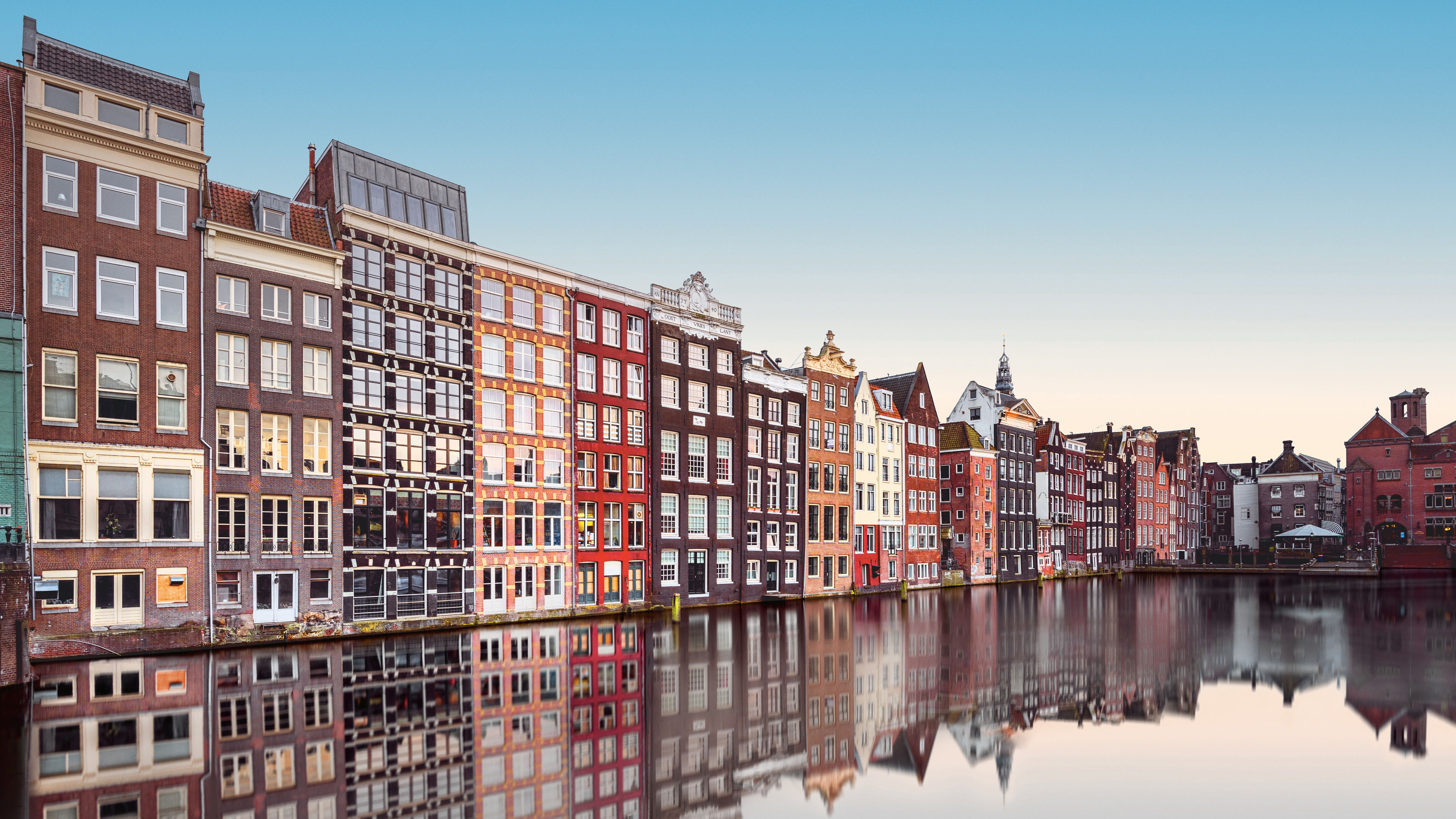 Bunte Häuser am Kanal in Amsterdam, spiegelnd im Wasser.