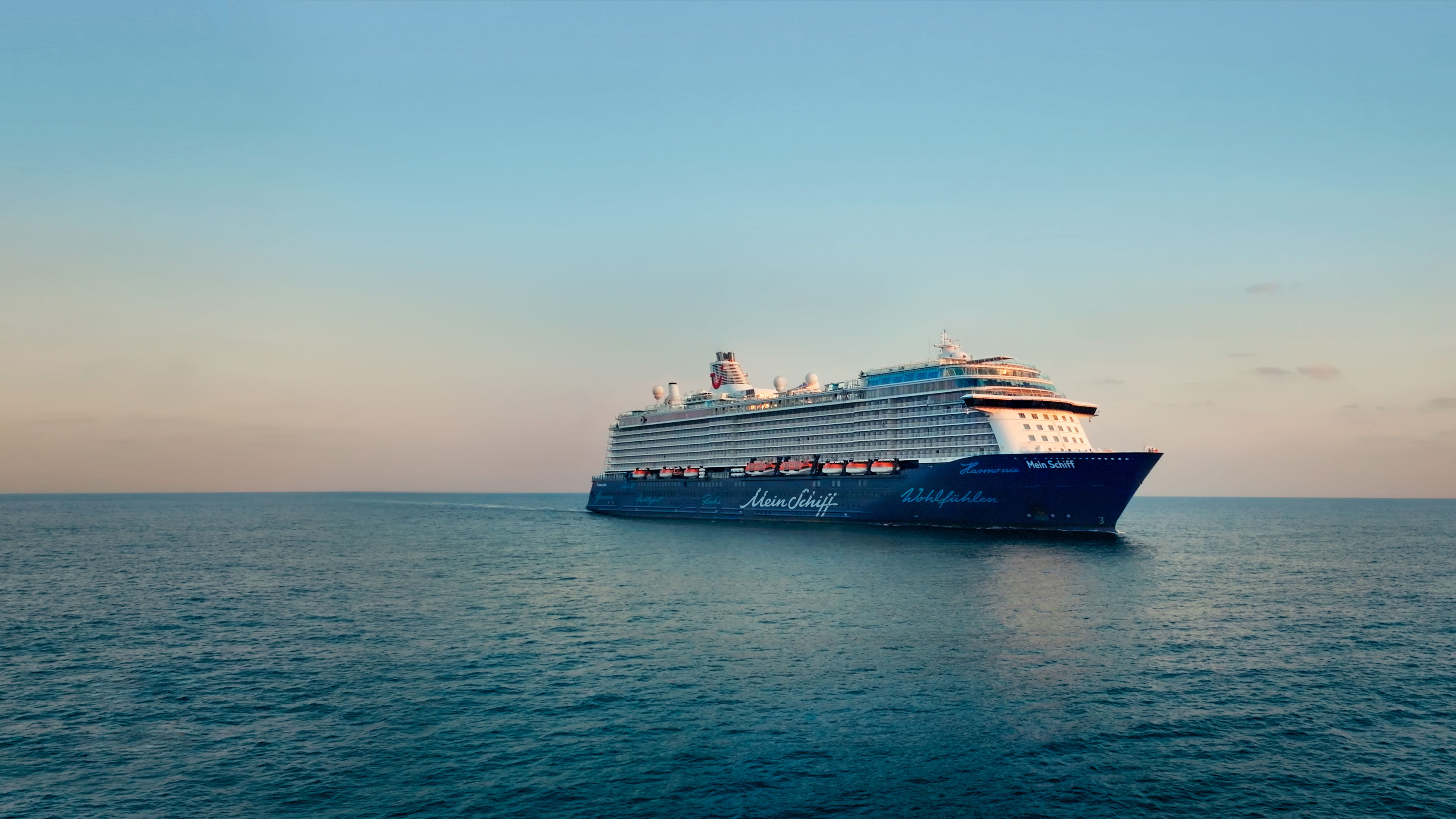 Kreuzfahrtschiff der Mein Schiff® Flotte auf offenem Meer bei Sonnenuntergang.