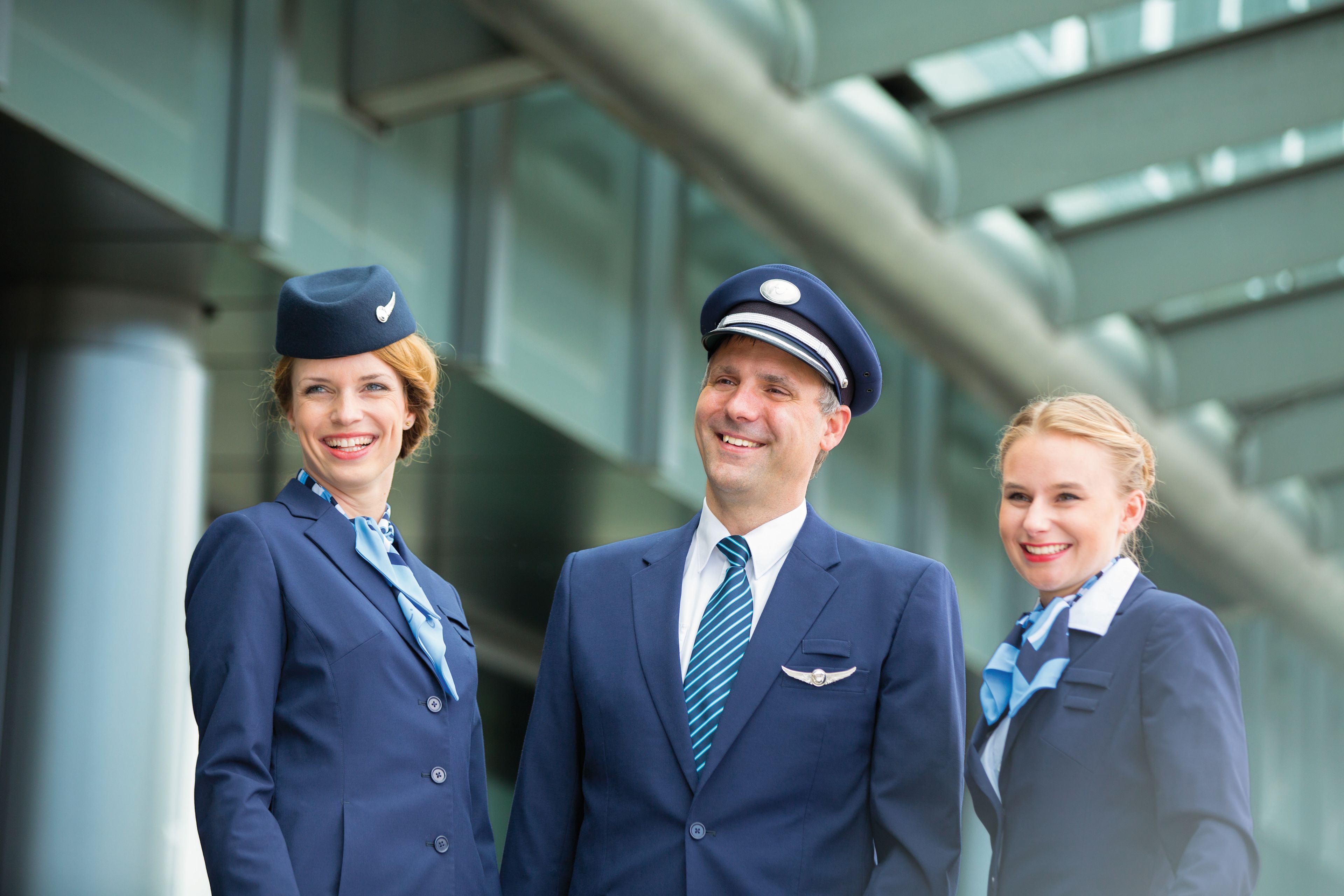 Flugbegleiter und Pilot in blauen Uniformen lächeln.