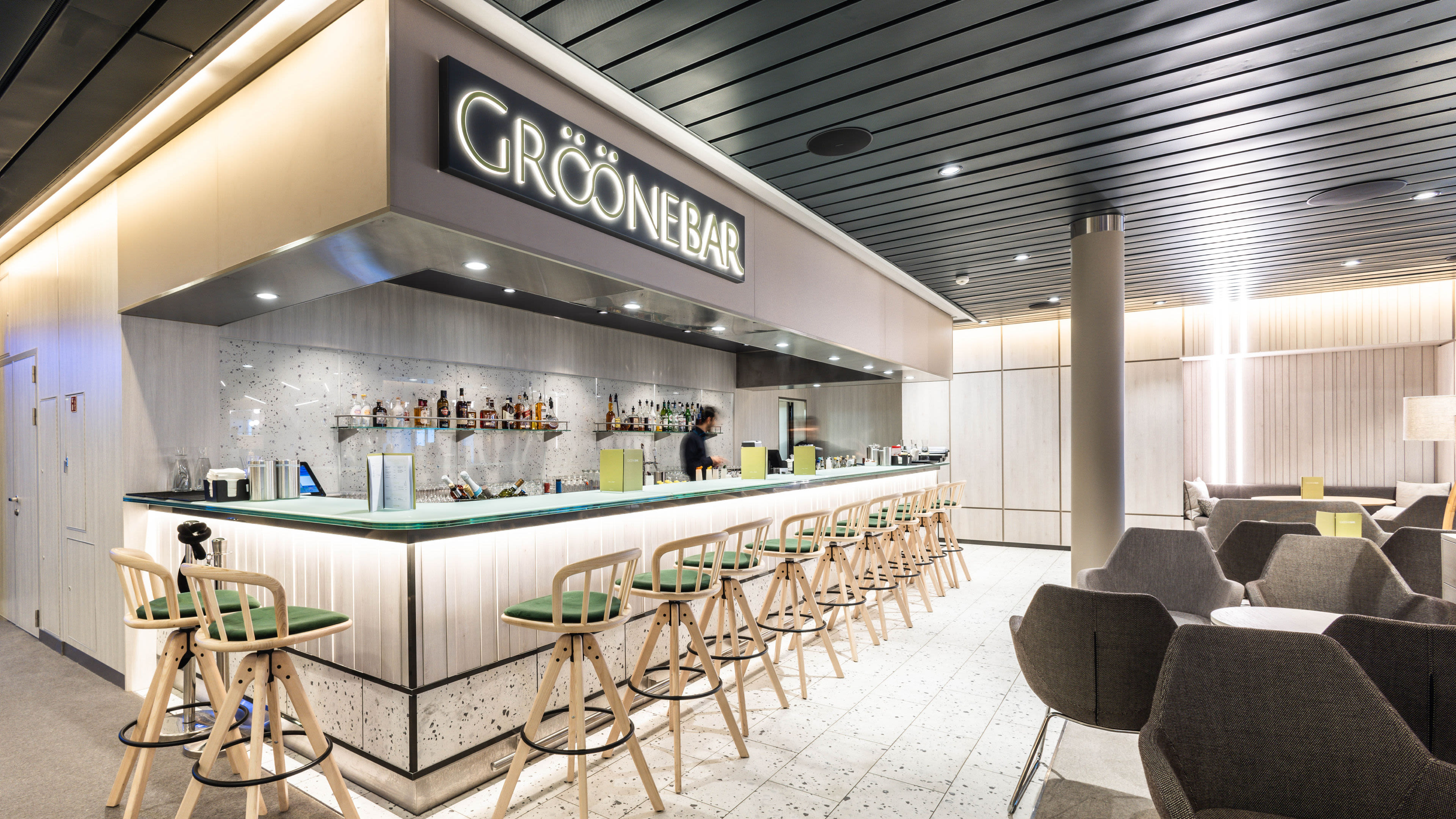 Moderne Bar mit grünen Hockern, beleuchtetem Tresen und gemütlichen Sitzbereichen.