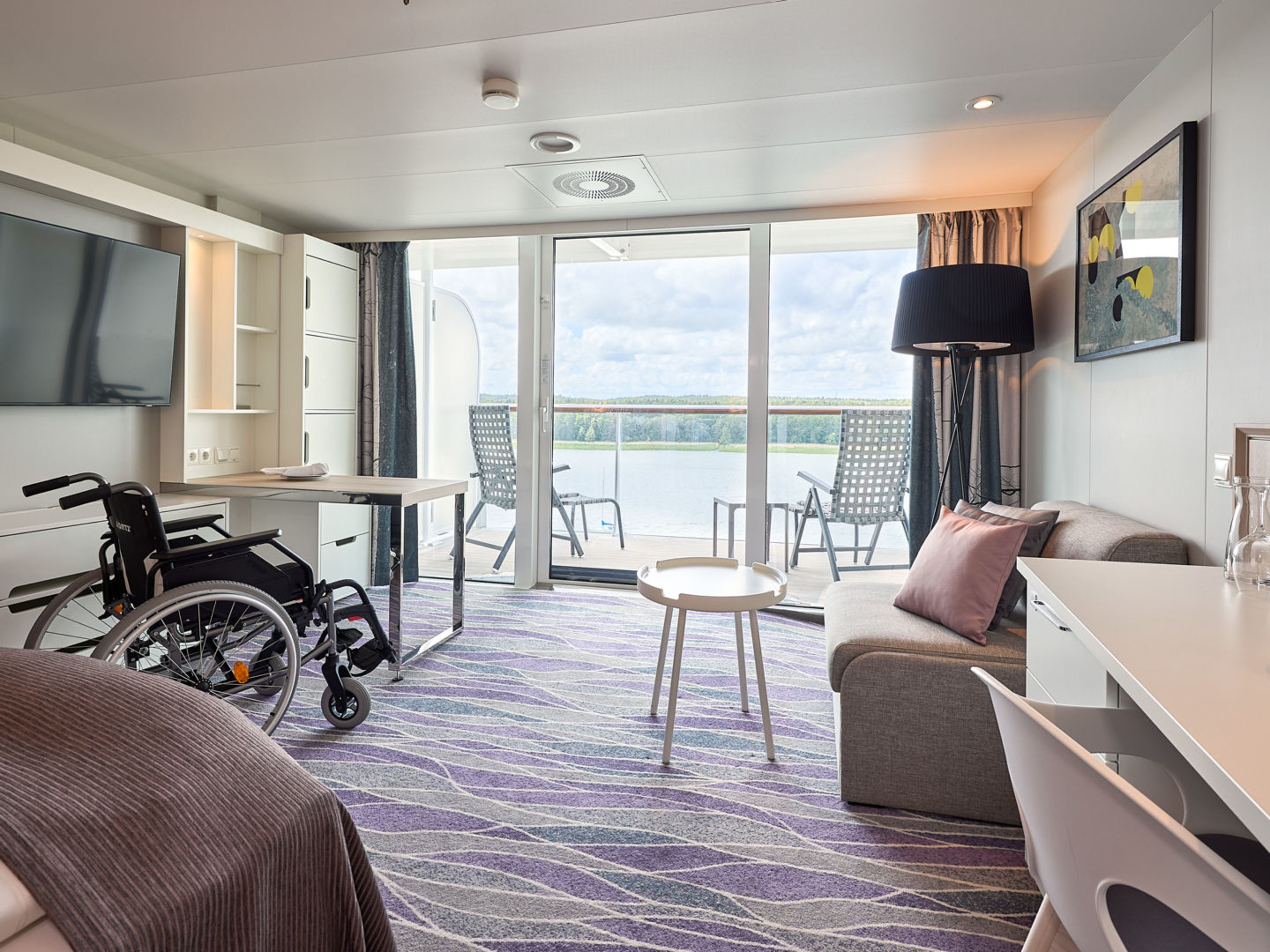 Barrierefreie Junior Suite auf der Mein Schiff 7 Rollstuhlgerechte Kabine mit Balkon, modern eingerichtet, lila Teppich.