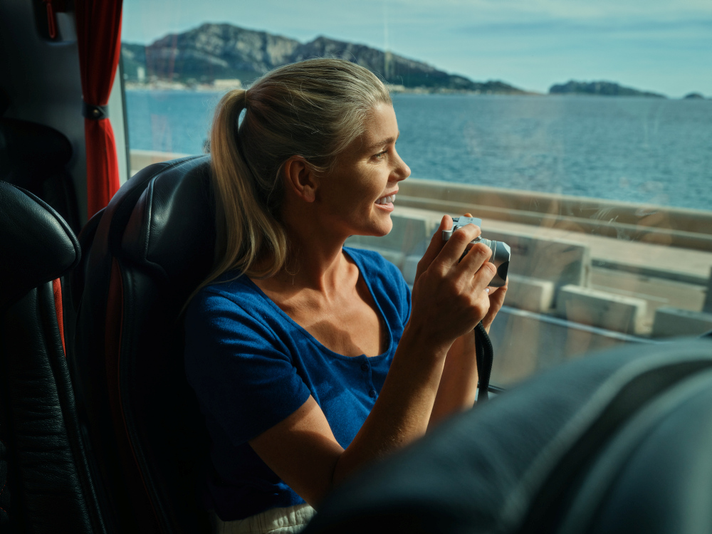 Frau im Bus mit Kamera, Meerblick, sonniger Tag.