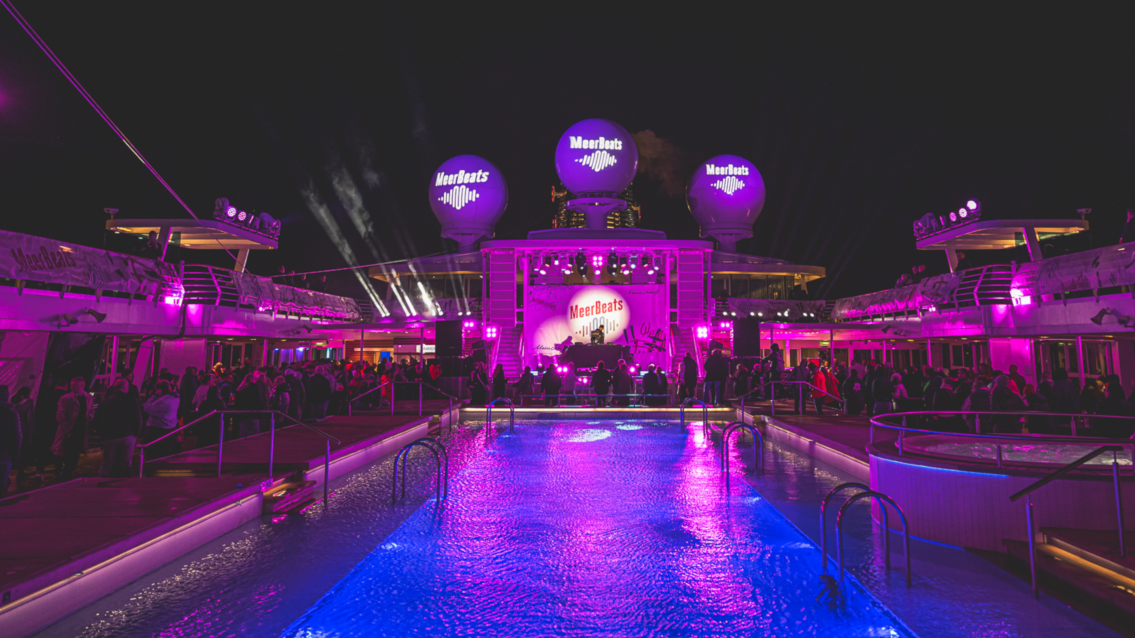 Nachtparty auf Kreuzfahrtschiff der Mein Schiff® Flotte, lila Beleuchtung, Pool, Menschenmenge.