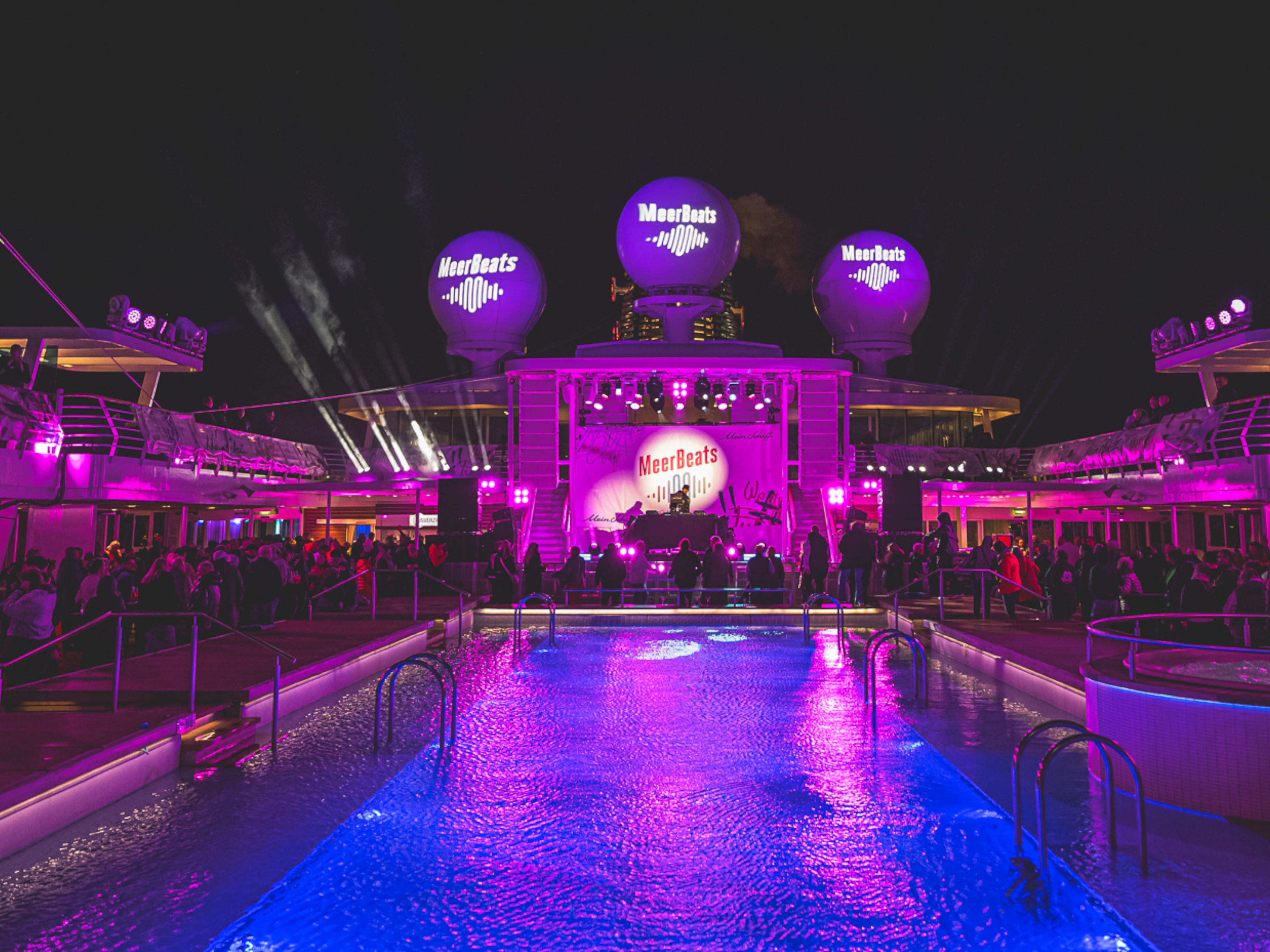 MeerBeats Nachtparty auf Kreuzfahrtschiff der Mein Schiff® Flotte, lila Beleuchtung, Pool, Menschenmenge.