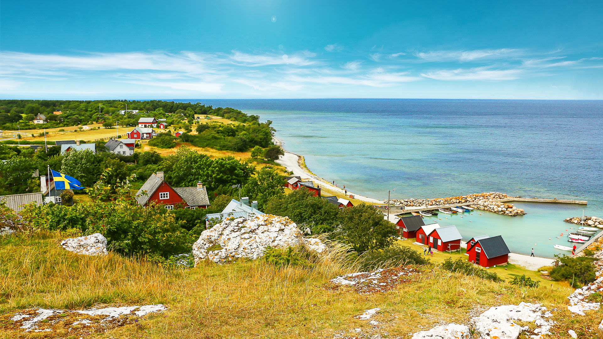 Schwedische Küstenlandschaft mit roten Häusern, blauem Meer und grünen Wiesen.