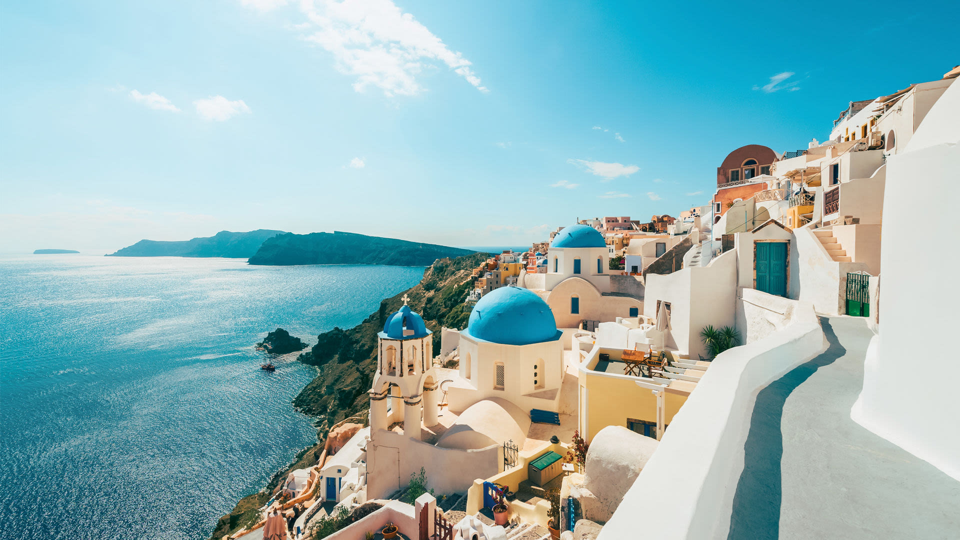 Santorini, weiße Gebäude, blaue Kuppeln, Meerblick, sonniger Himmel.
