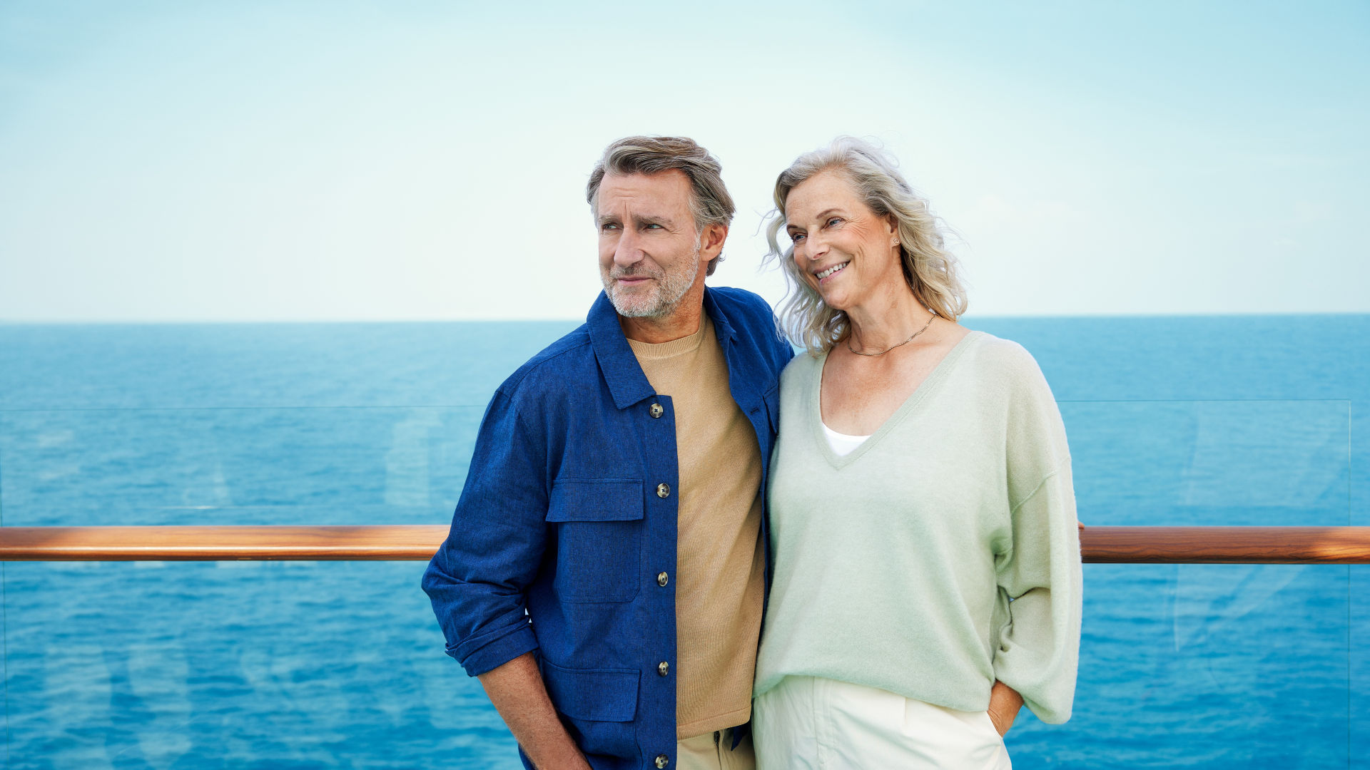 Paar auf Kreuzfahrtschiff, lächelnd, blauer Himmel, Meereshorizont.