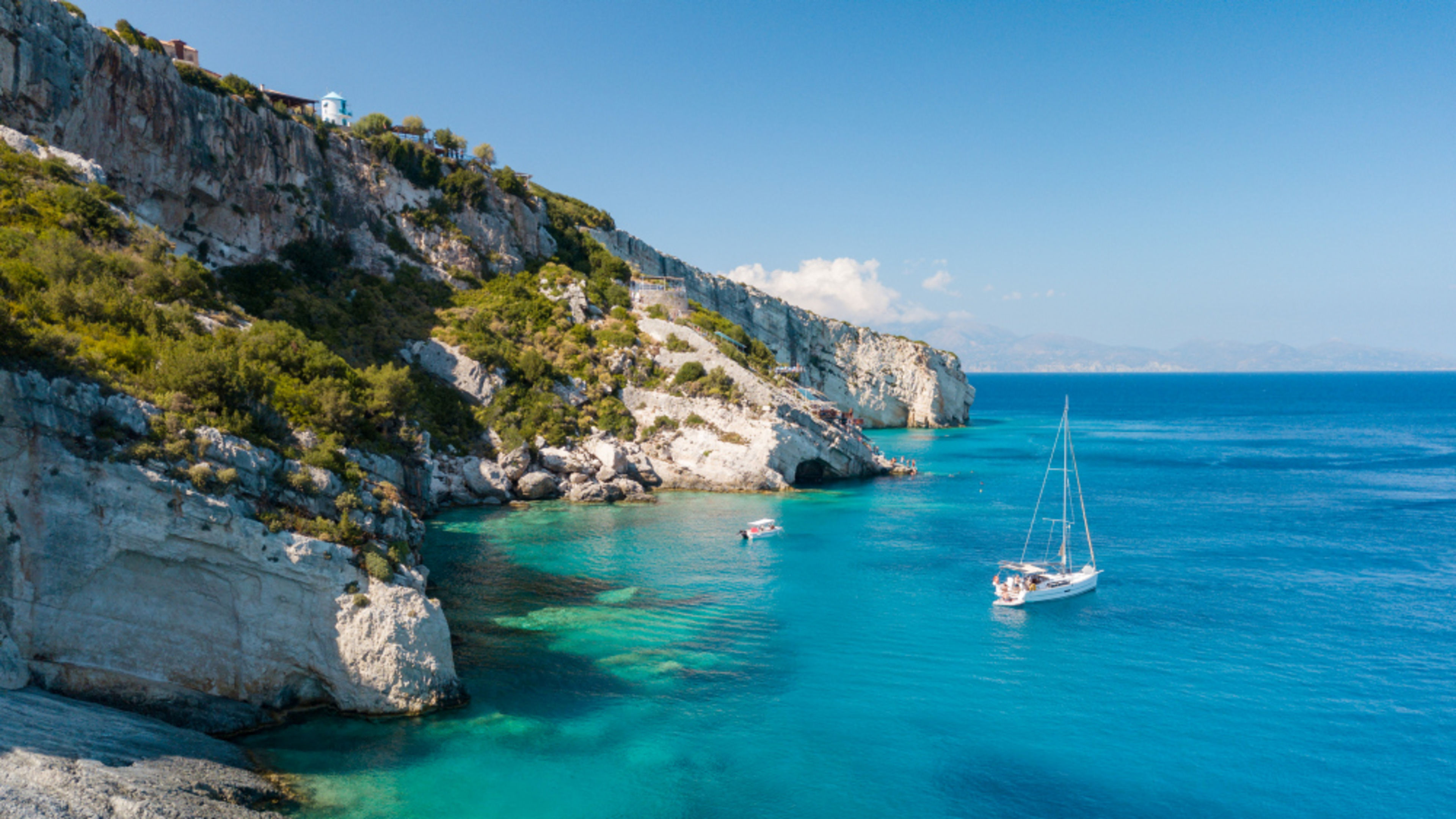Bucht Griechenland Mittelmeer Segelboot im türkisblauen Wasser vor felsiger Küste, sonniger Himmel.