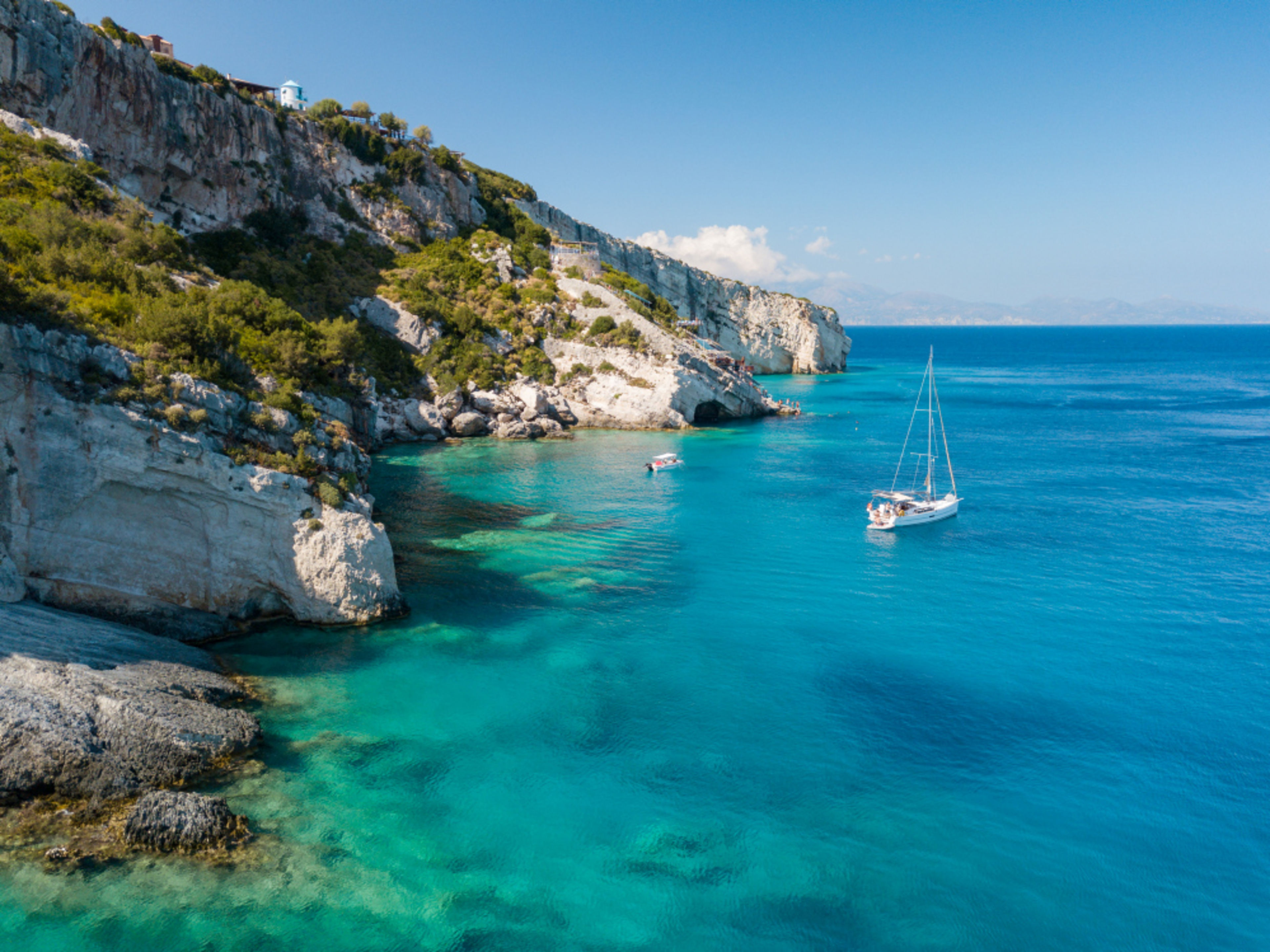 Bucht Griechenland Mittelmeer Segelboot im türkisblauen Wasser vor felsiger Küste, sonniger Himmel.