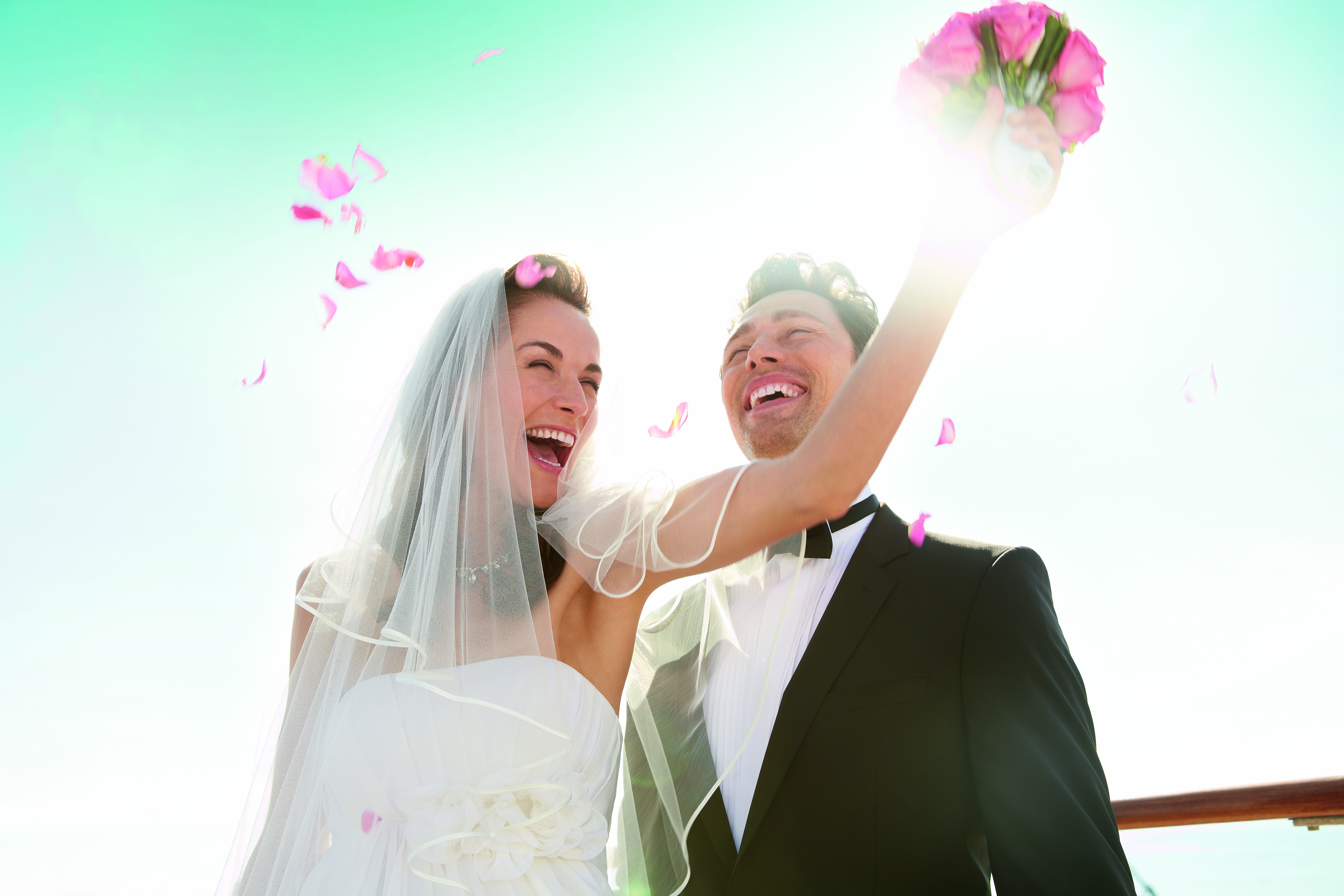 Lachendes Brautpaar mit Blumenstrauß und Sonnenlicht.