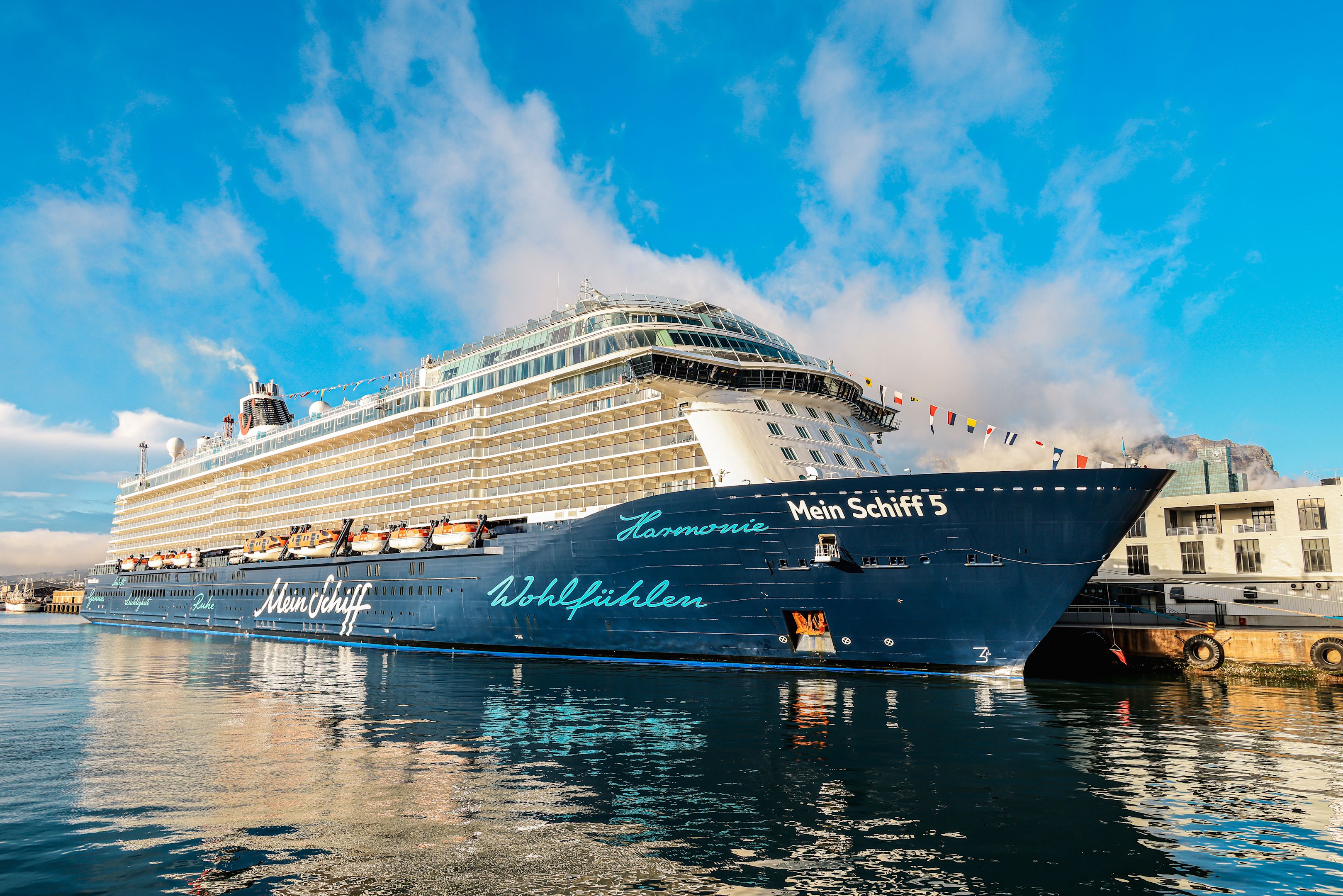 Kreuzfahrtschiff der Mein Schiff® Flotte im Hafen, blauer Himmel.