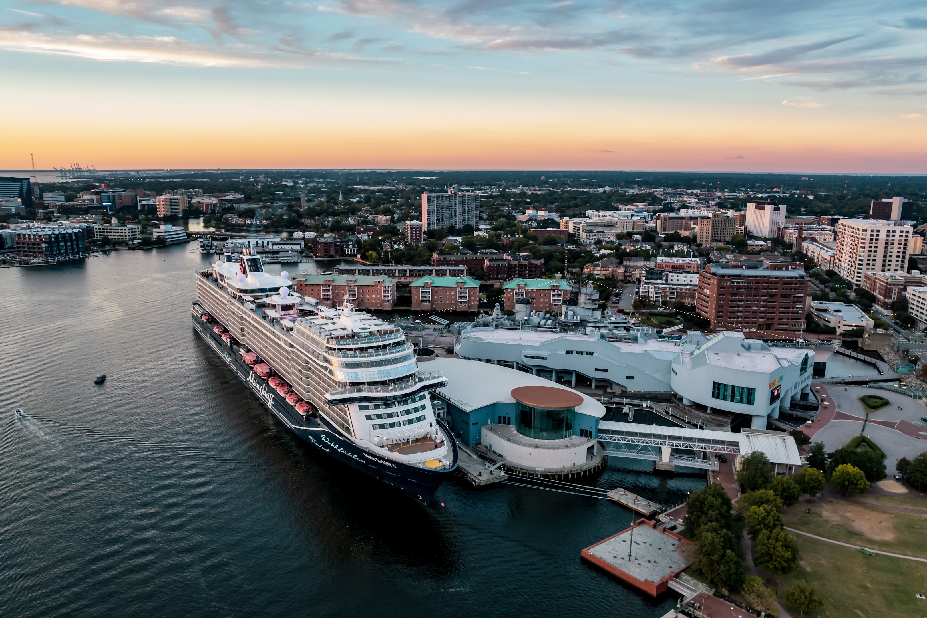 Kreuzfahrtschiff der Mein Schiff® Flotte im Hafen bei Sonnenuntergang, Stadt im Hintergrund.