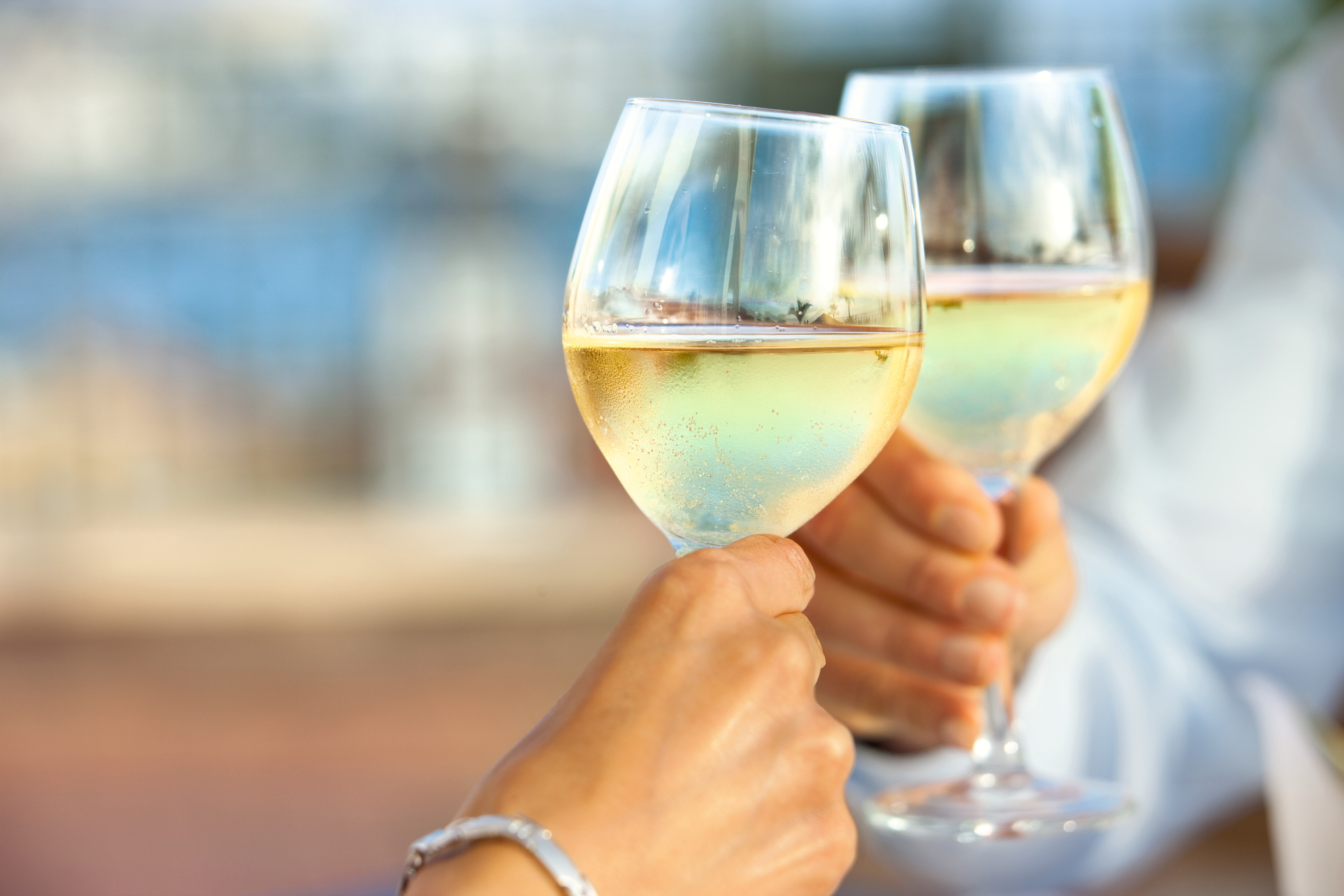 Zwei Personen stoßen mit Gläsern Weißwein an.