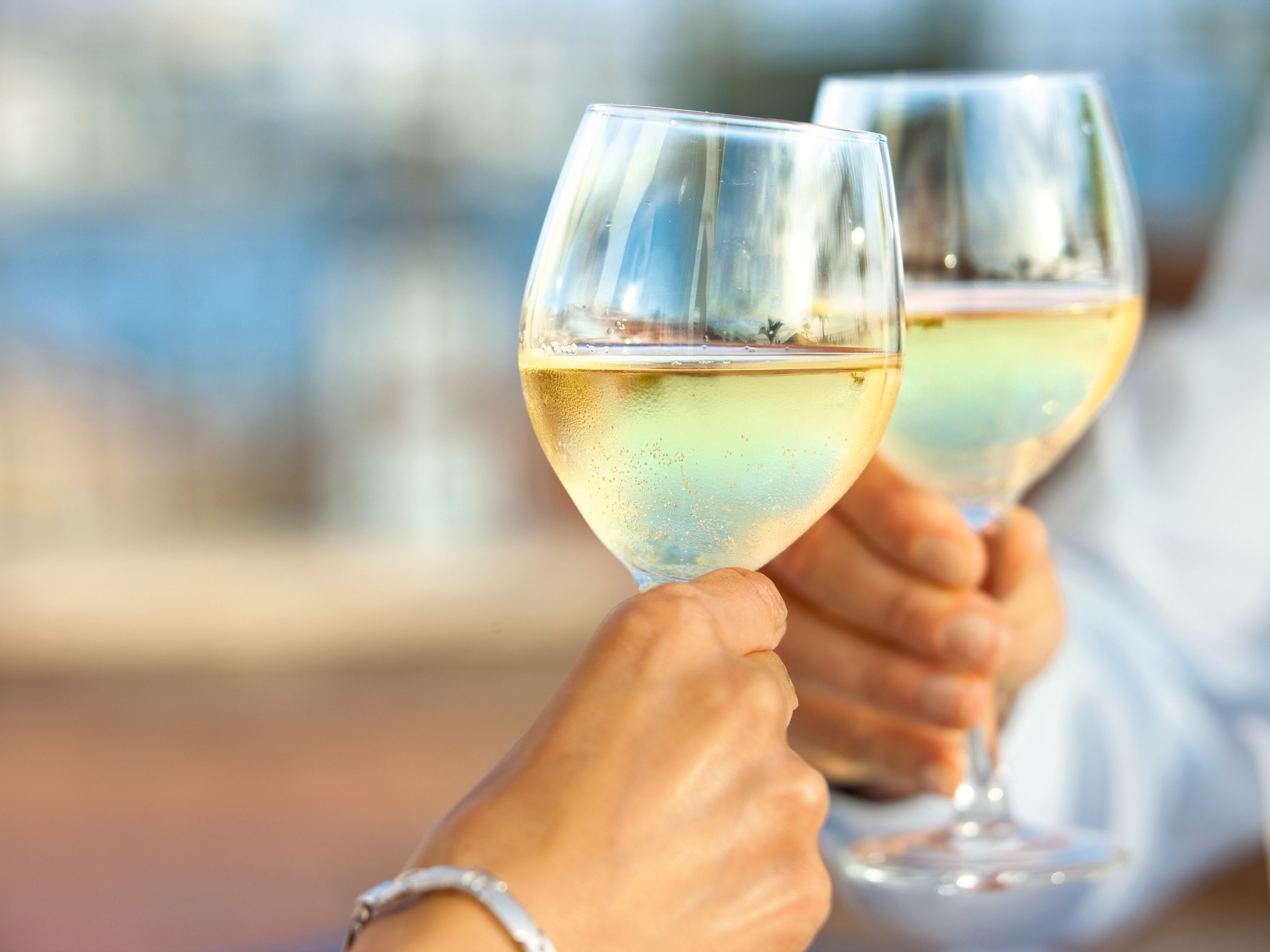 Anstoßen_mit_Wein Zwei Personen stoßen mit Gläsern Weißwein an.