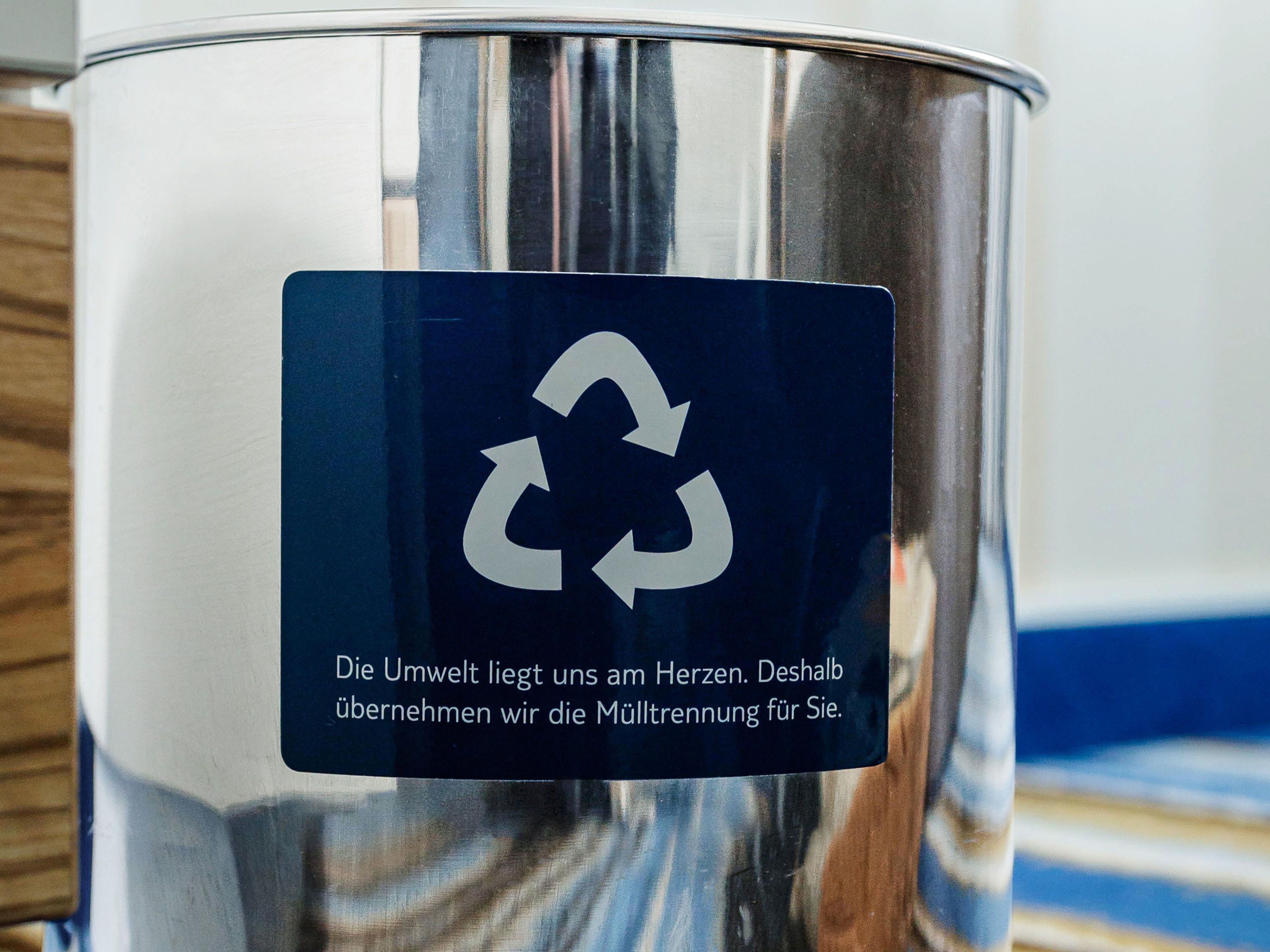 Nachhaltigkeit - Abfallmanagement Recycling-Symbol auf silbernem Mülleimer mit Holz- und Teppichhintergrund.