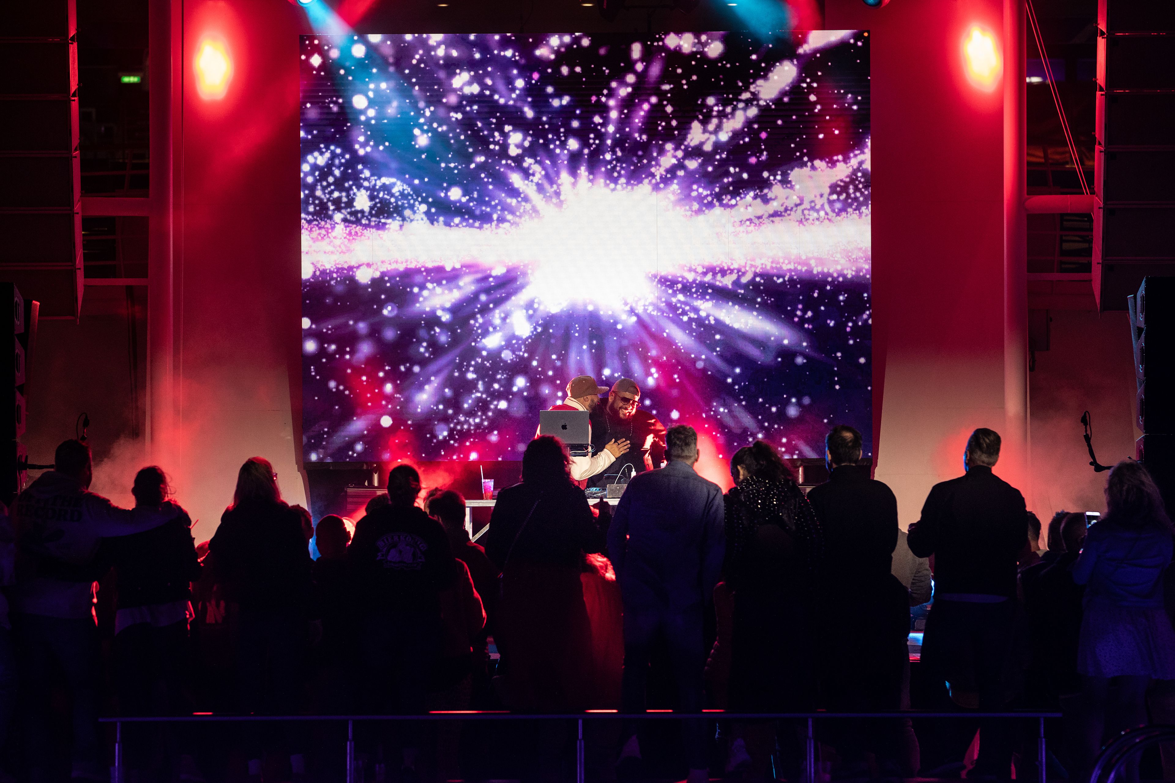 Menschenmenge vor bunter Bühne mit Lichteffekten und DJ.